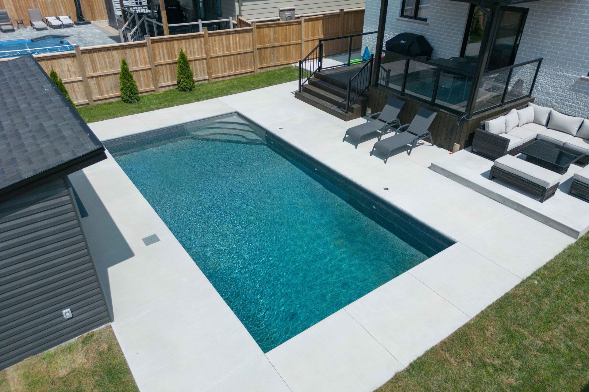 Modern backyard with a rectangular swimming pool, patio lounge chairs, and a glass-walled house