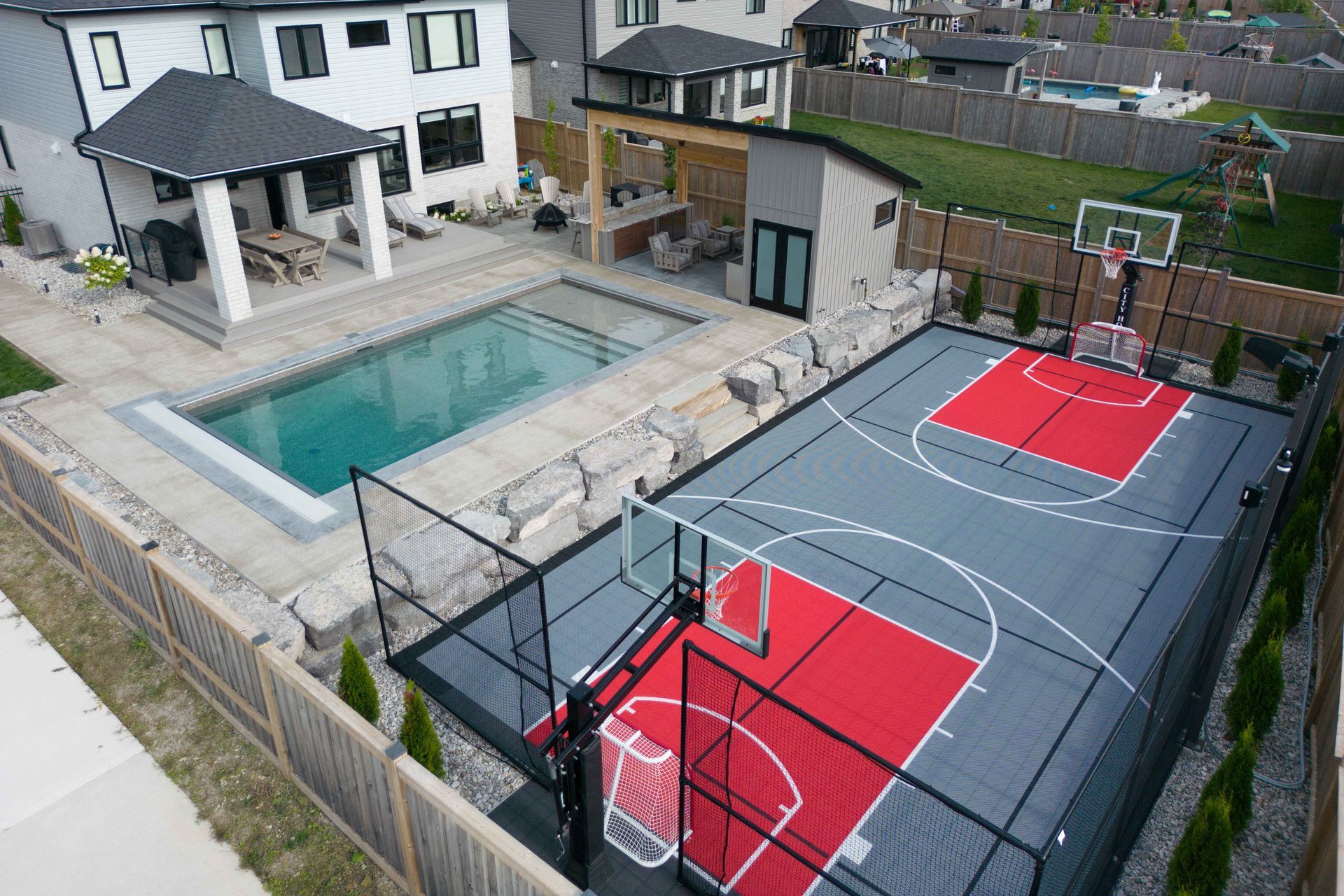 Backyard with swimming pool and fenced red-and-gray sports court beside a house