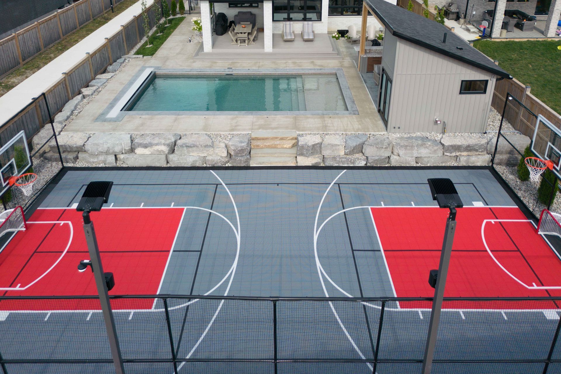 Rooftop basketball court with two red half-courts beside a swimming pool and modern buildings.