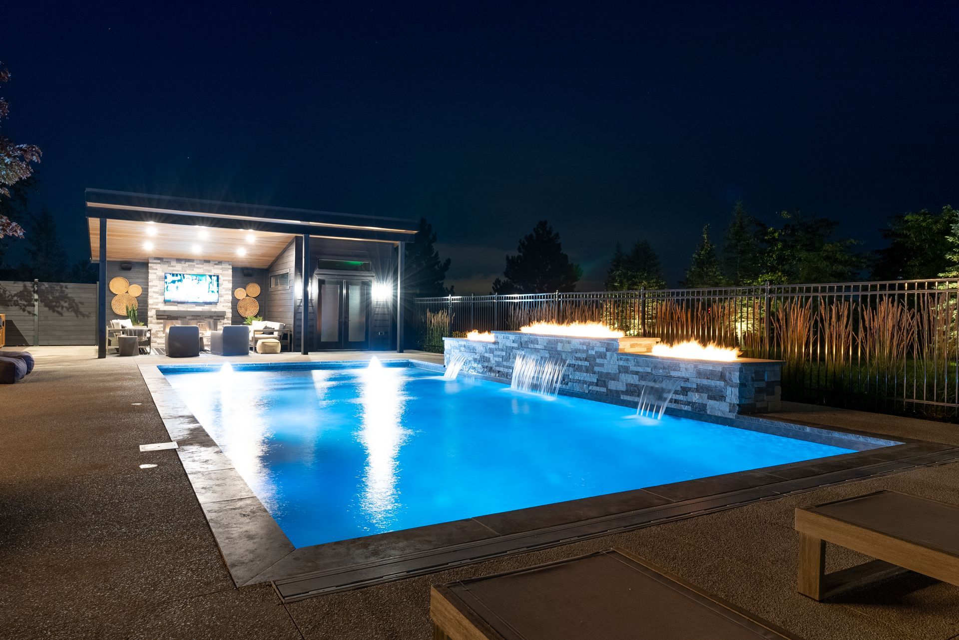 Illuminated backyard pool at night beside a modern patio and lounge area