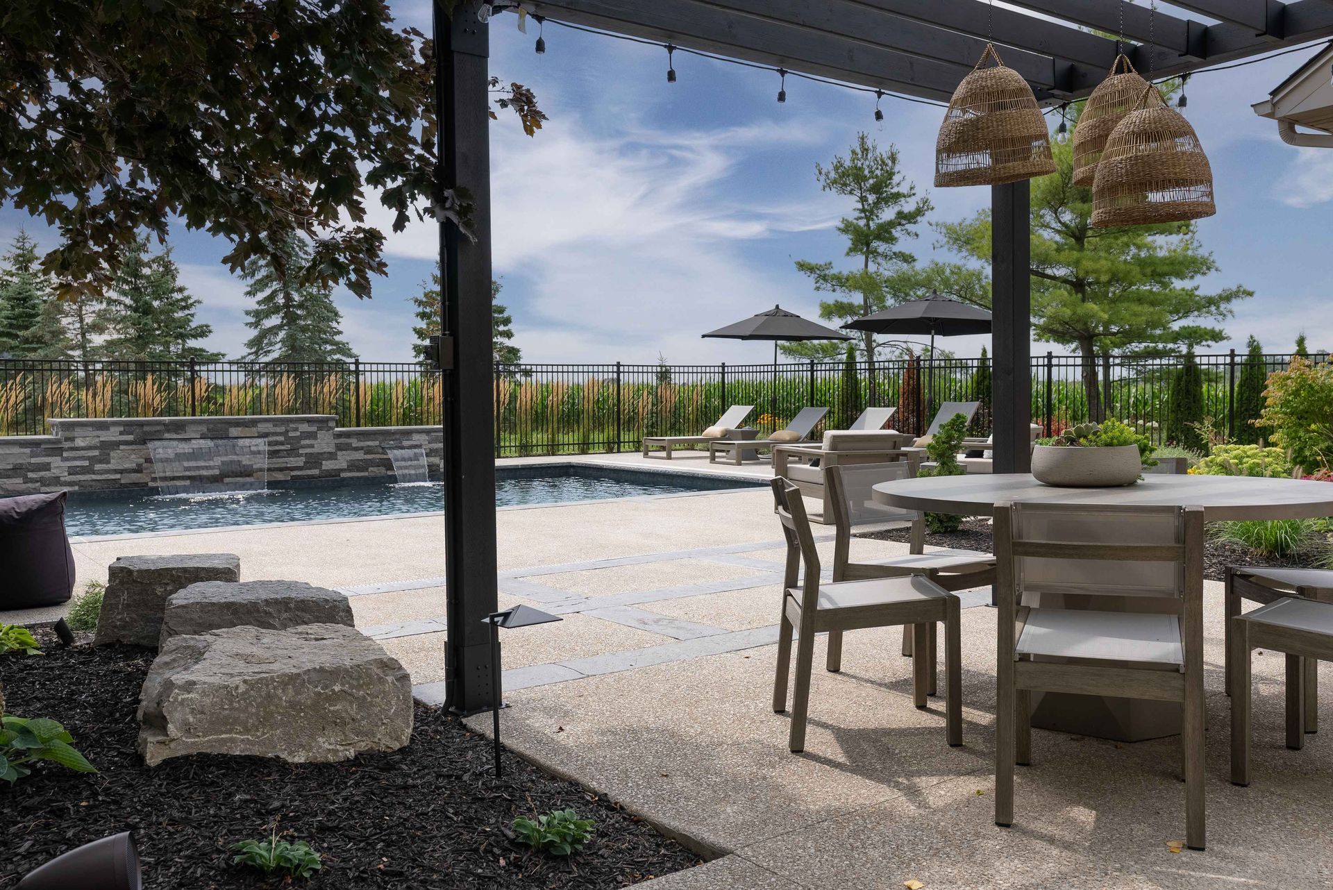 Outdoor patio with table and chairs beside a pool, framed by a shaded pergola and ocean view