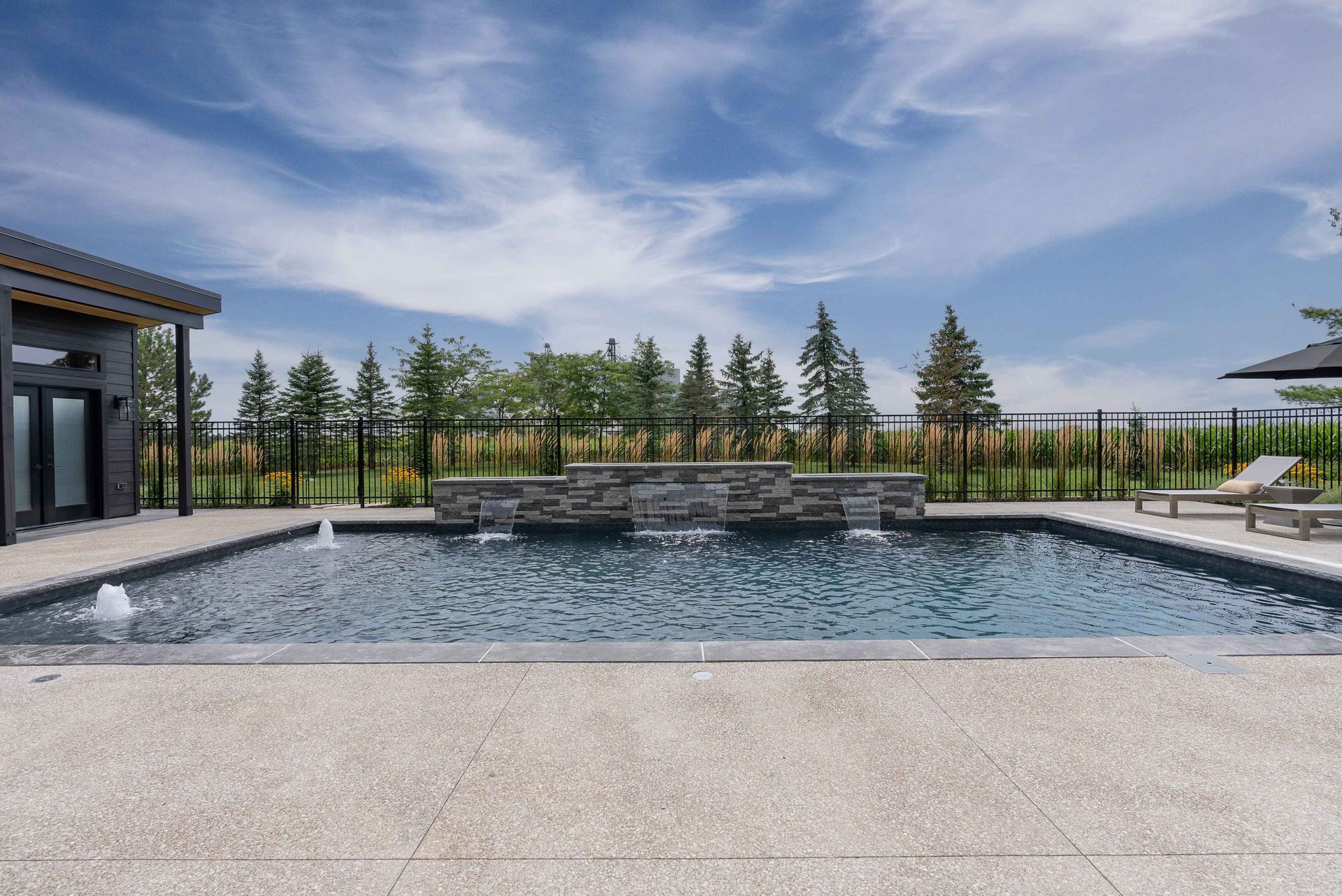 Modern backyard pool with stone waterfall, lounge chairs, and mountain view under a blue sky