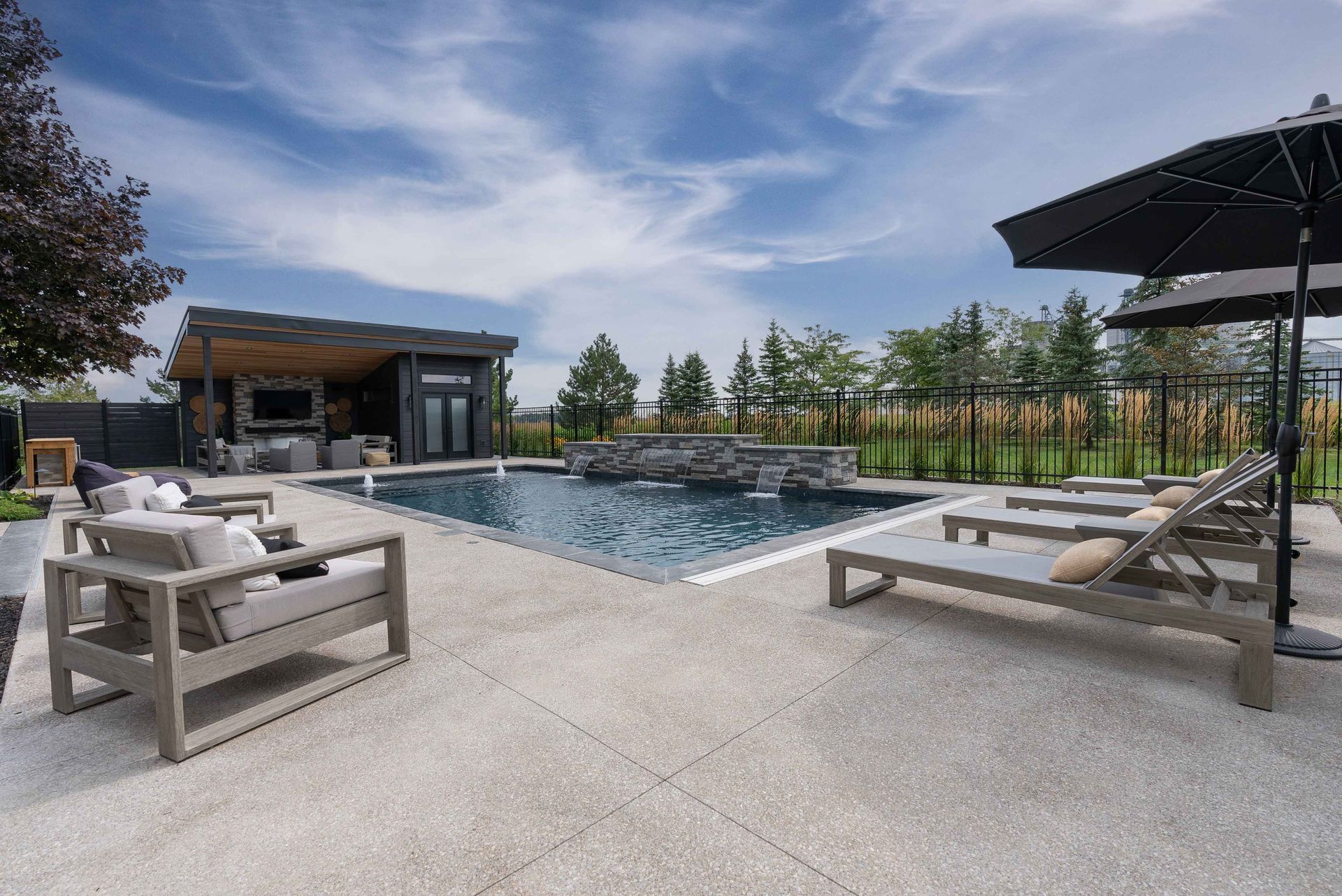 Modern backyard pool with lounge chairs, pergola, and blue sky on a sunny day