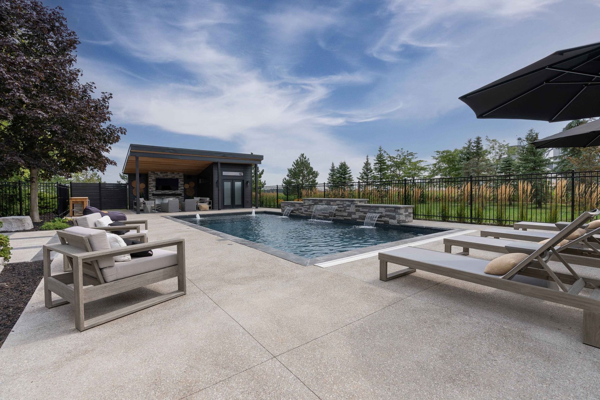 Modern outdoor patio with a rectangular pool, lounge chairs, and a covered seating area under a blue sky