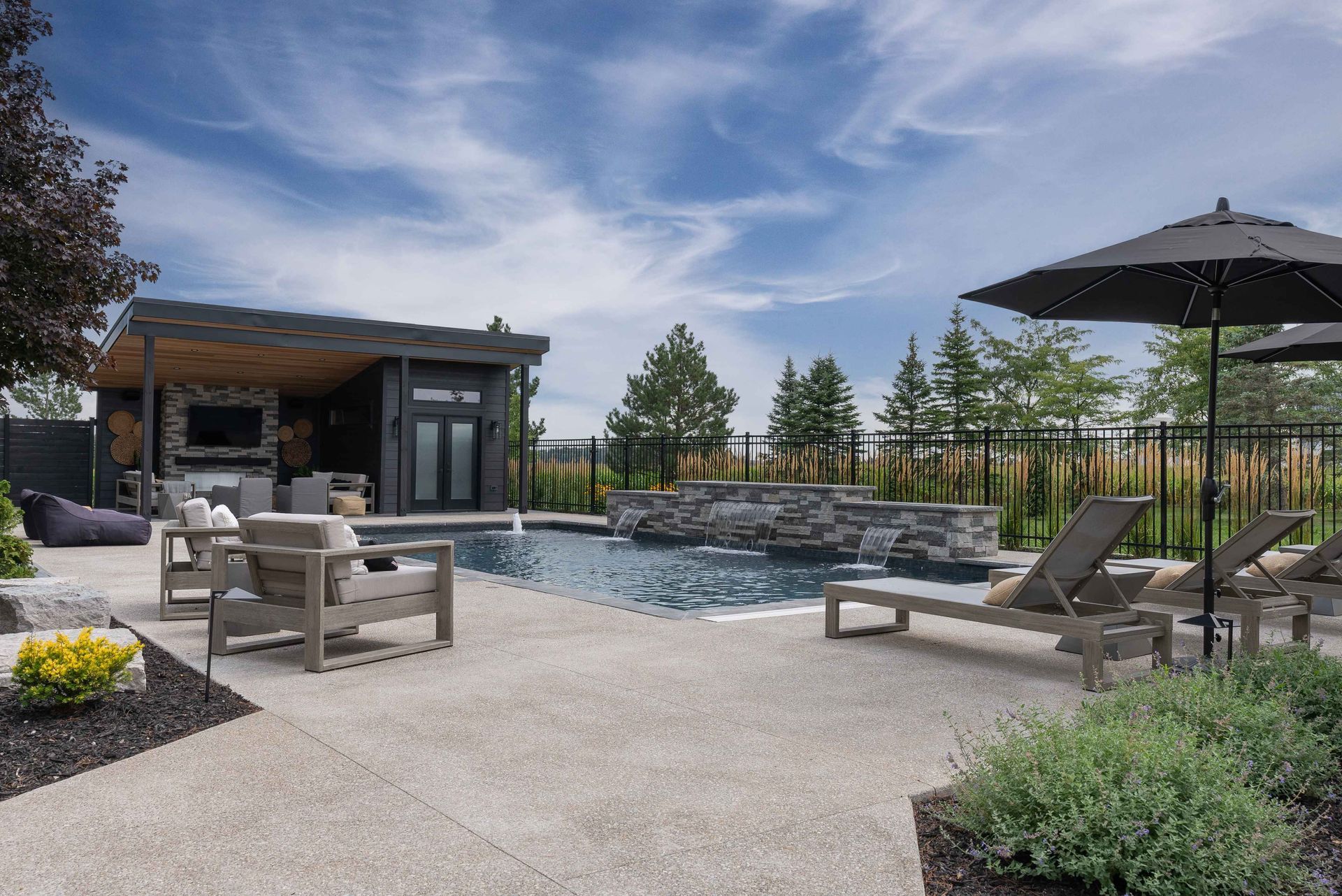 Backyard patio with pool, lounge chairs, umbrella, and modern outdoor seating near a small building