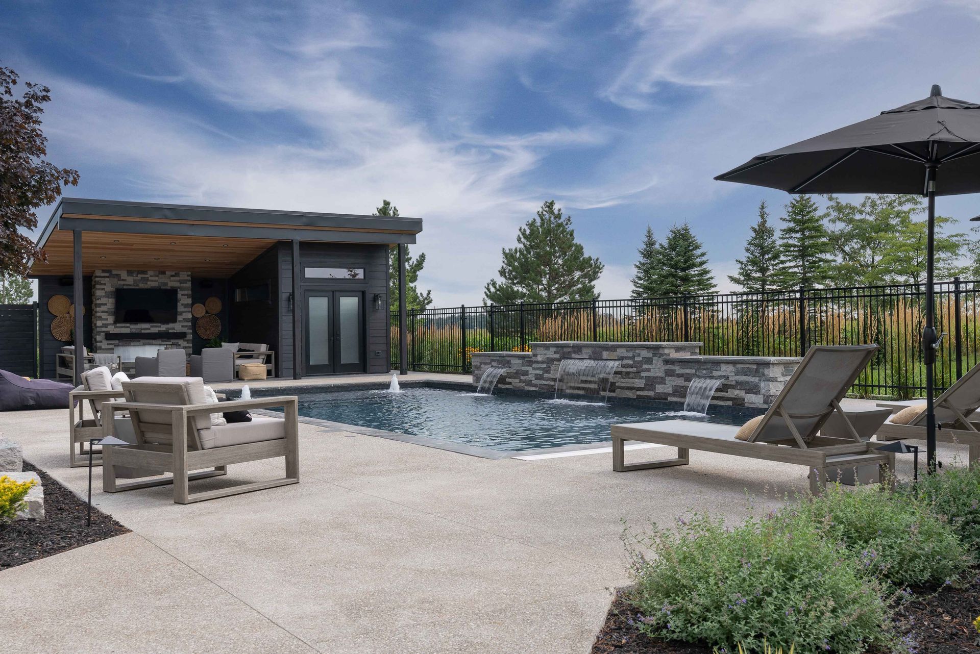 Modern backyard pool with lounge chairs, patio seating, and a small pool house under a clear sky