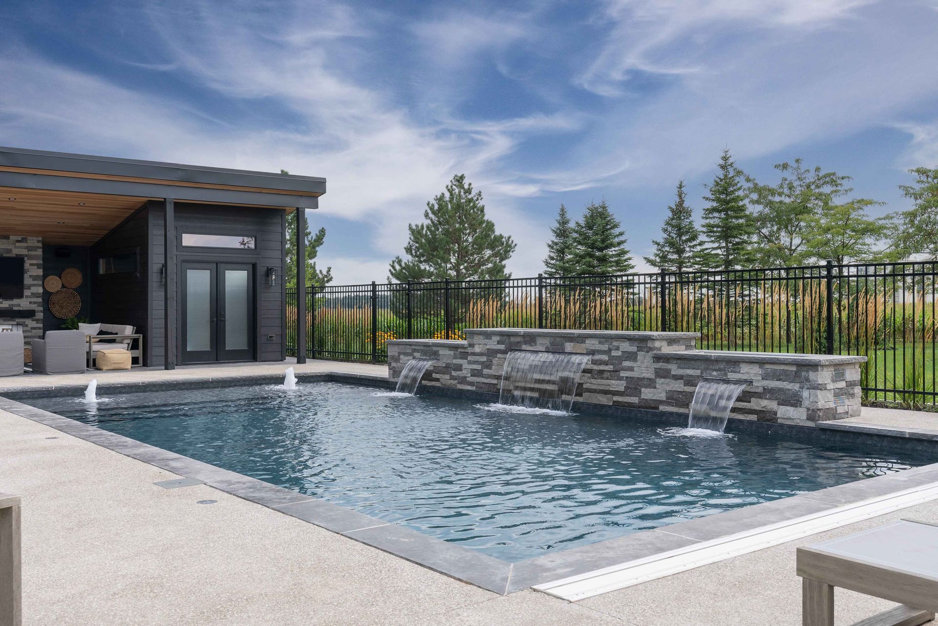 Modern backyard pool with stone waterfall wall and patio beside a house