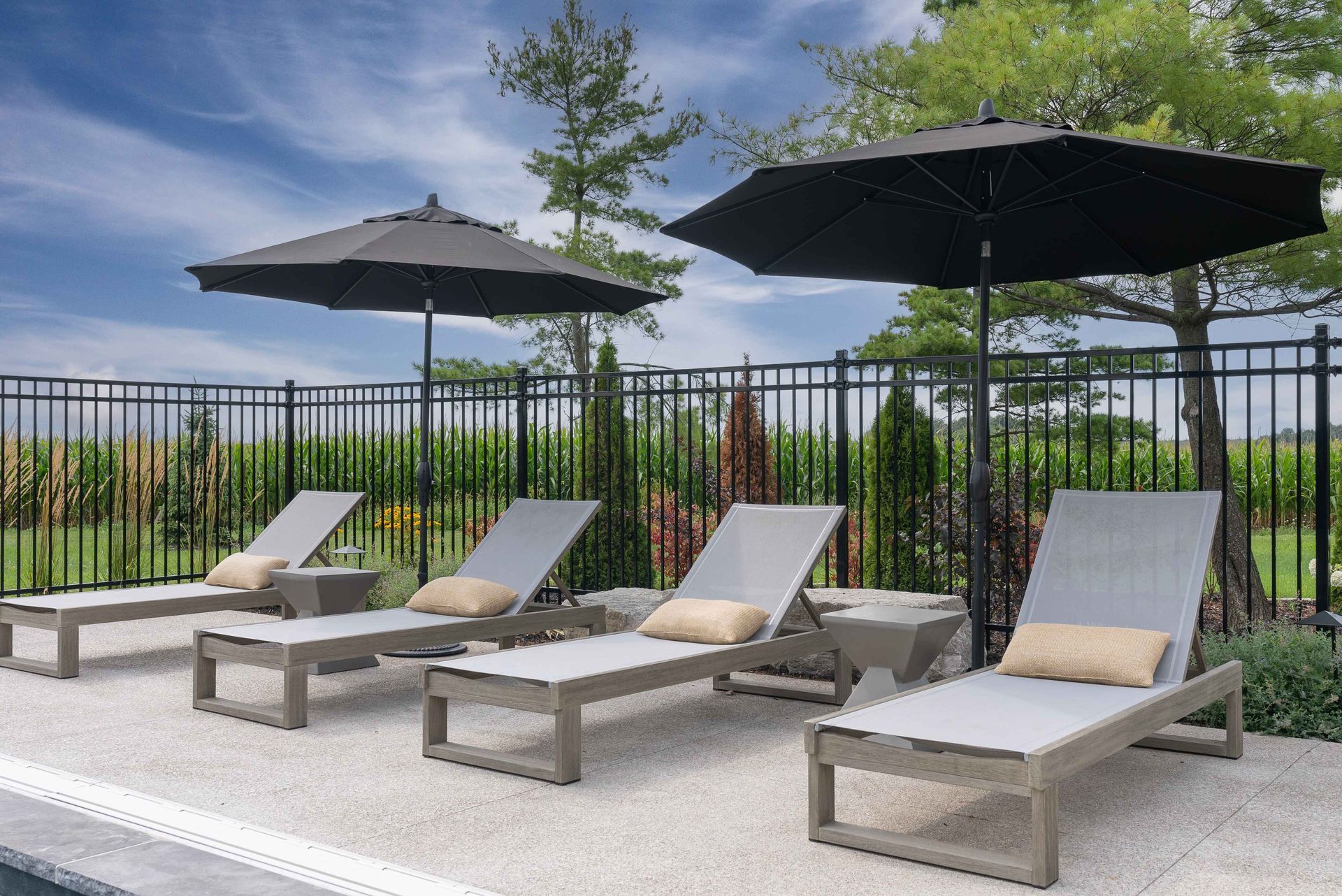 Poolside lounge chairs with black umbrellas beside a fenced outdoor area under a cloudy sky