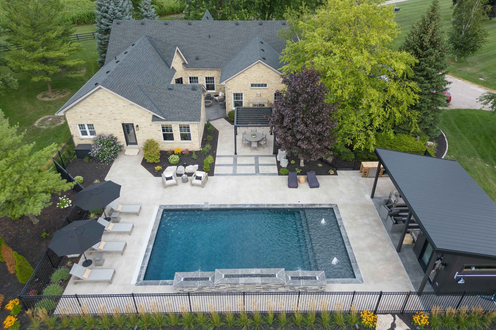 Aerial view of a beige house with a backyard pool, patio seating, and landscaped yard