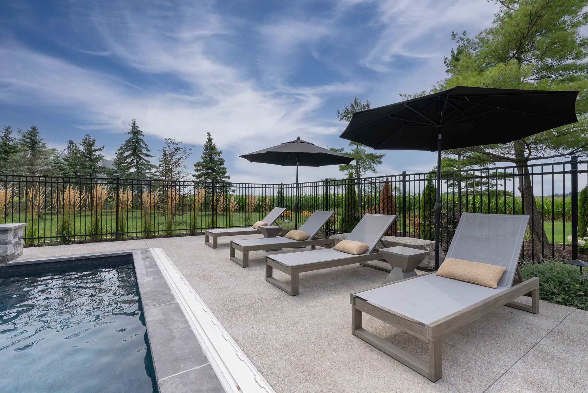 Poolside lounge chairs under umbrellas beside a modern swimming pool on a sunny day