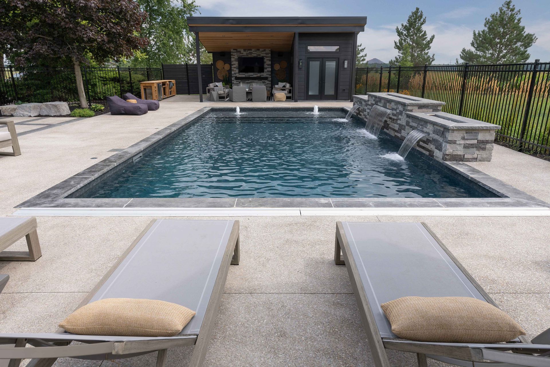 Backyard pool with two lounge chairs in front of a modern patio and stone water feature
