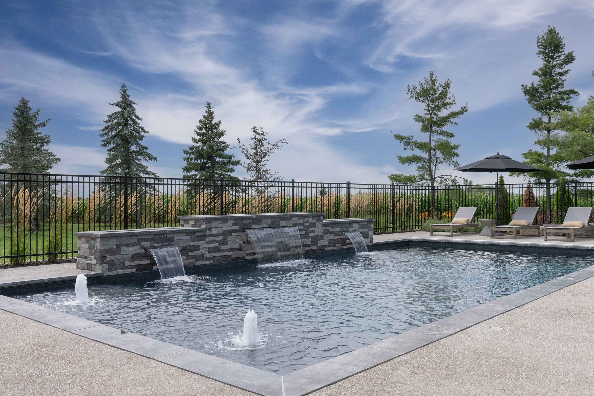 Modern outdoor pool with stone waterfall and lounge chairs under a blue sky