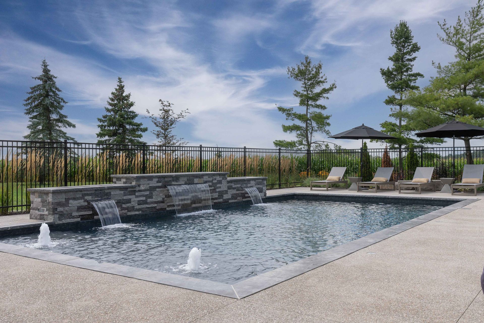Outdoor pool with stone water feature, lounge chairs, and pergola under a blue sky
