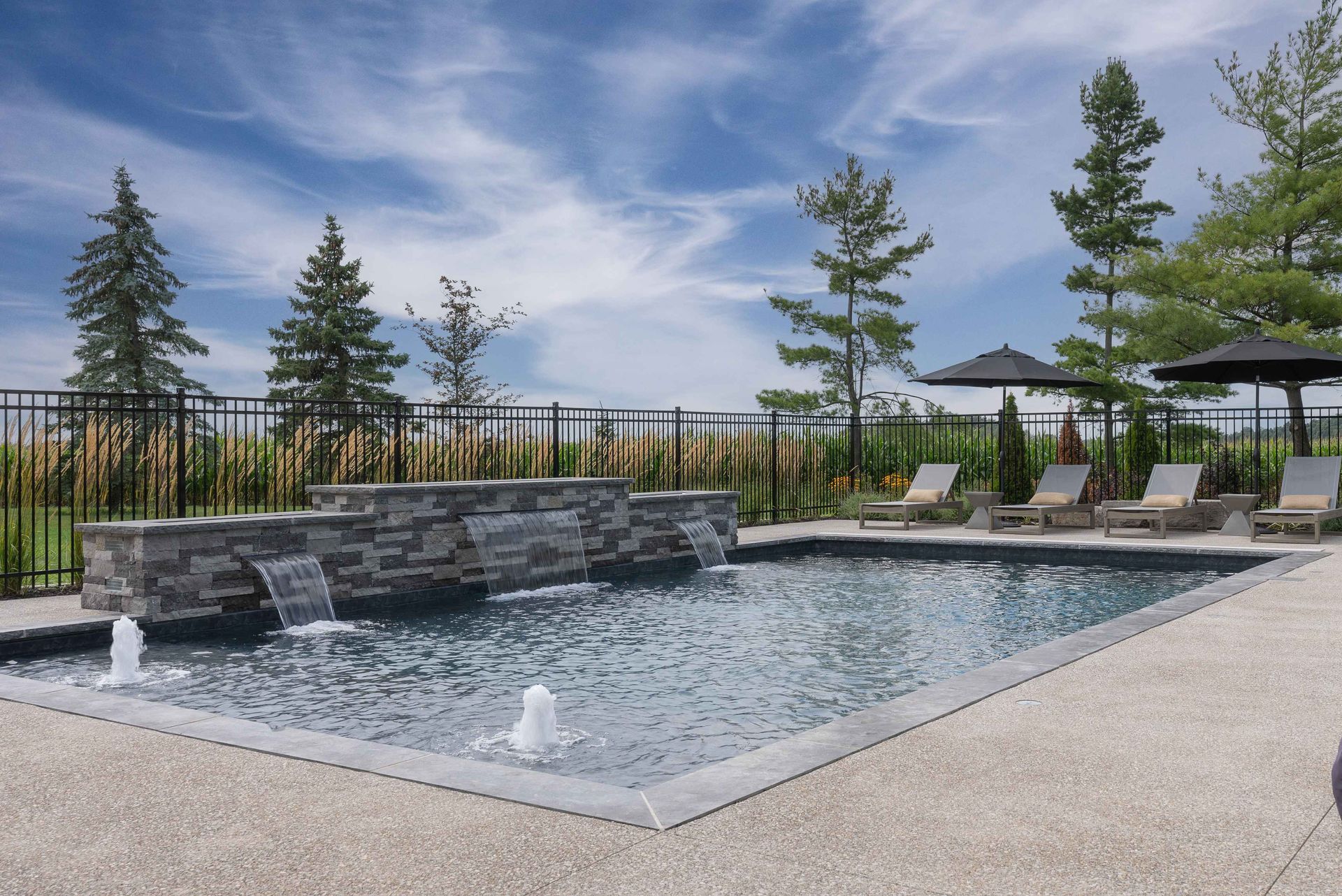 Outdoor pool with stone waterfall, lounge chairs, and pergola under a blue sky
