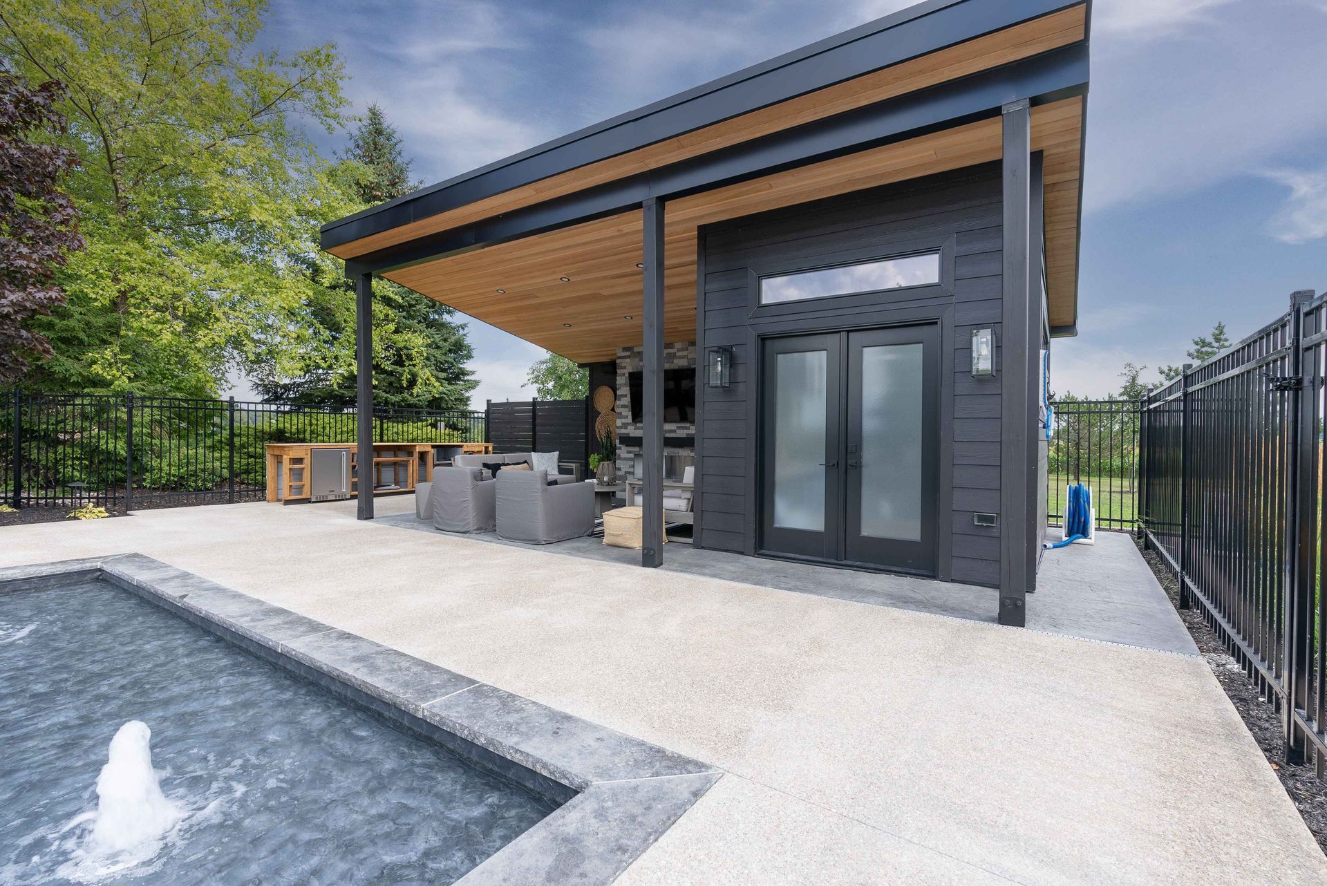 Modern poolside patio with a dark-gray outdoor kitchen and slanted wood-roof pavilion.