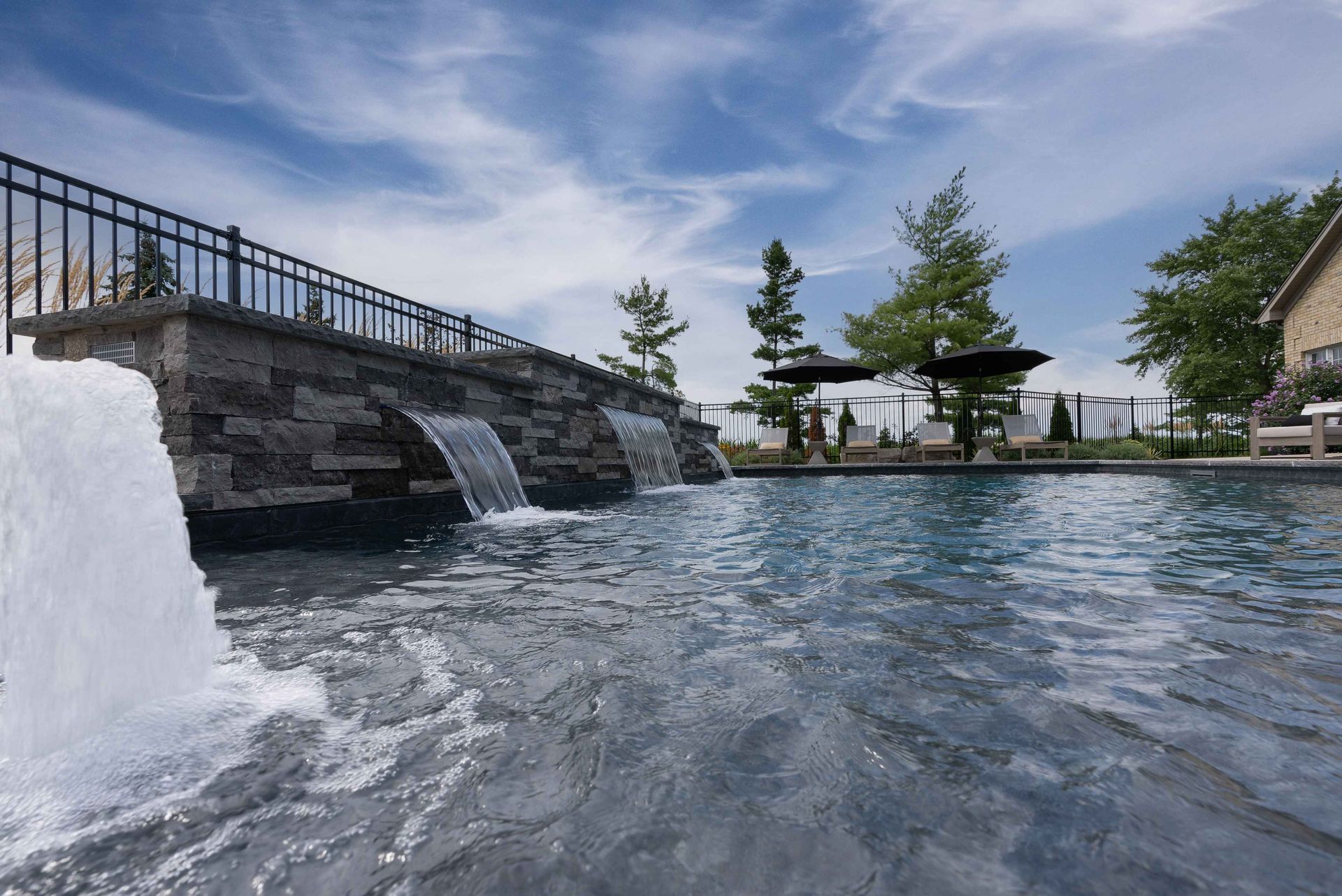 Pool with stone waterfall, lounge chairs, and cabanas under a blue sky.