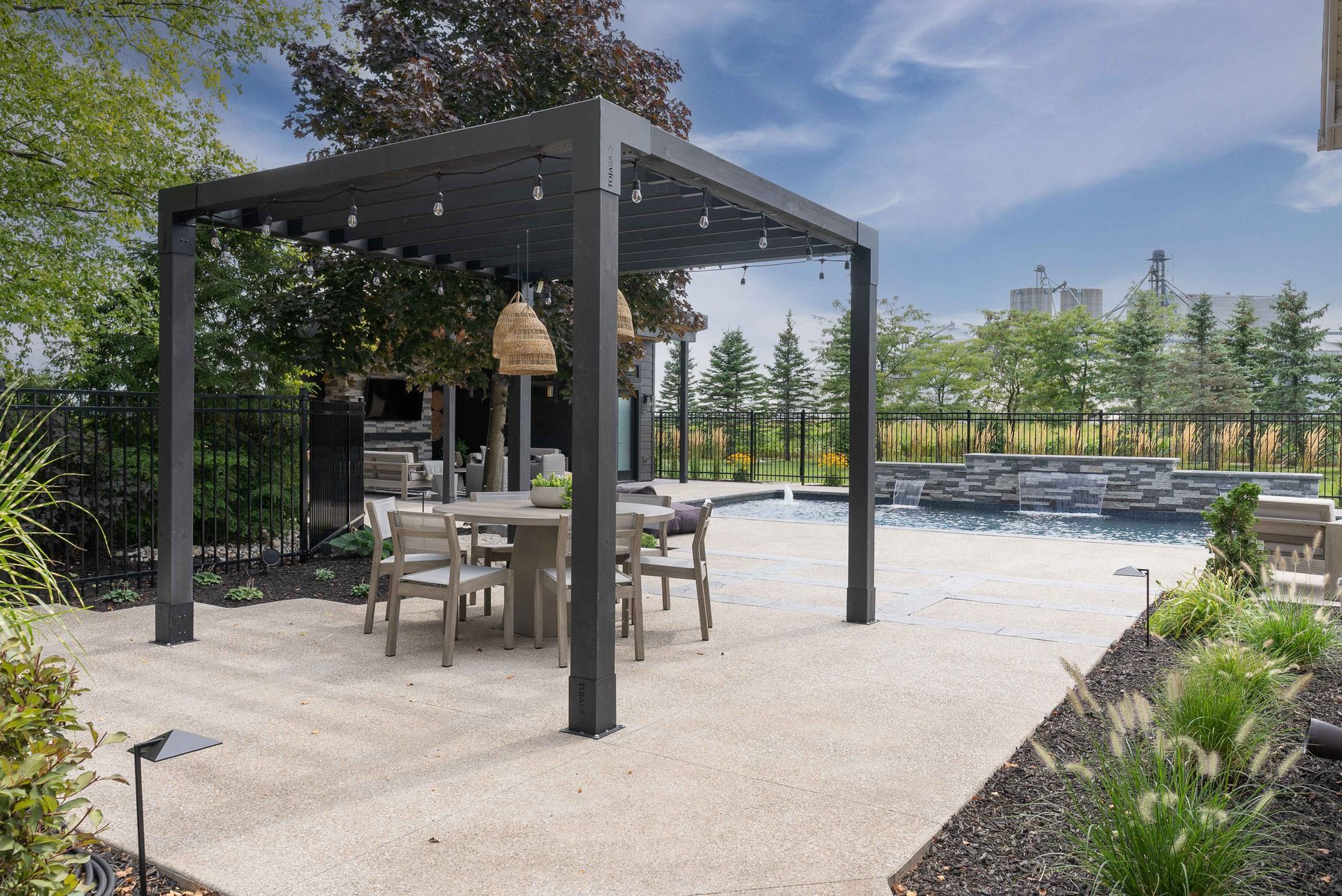 Outdoor patio with a pergola, table and chairs, surrounded by greenery and gravel landscaping