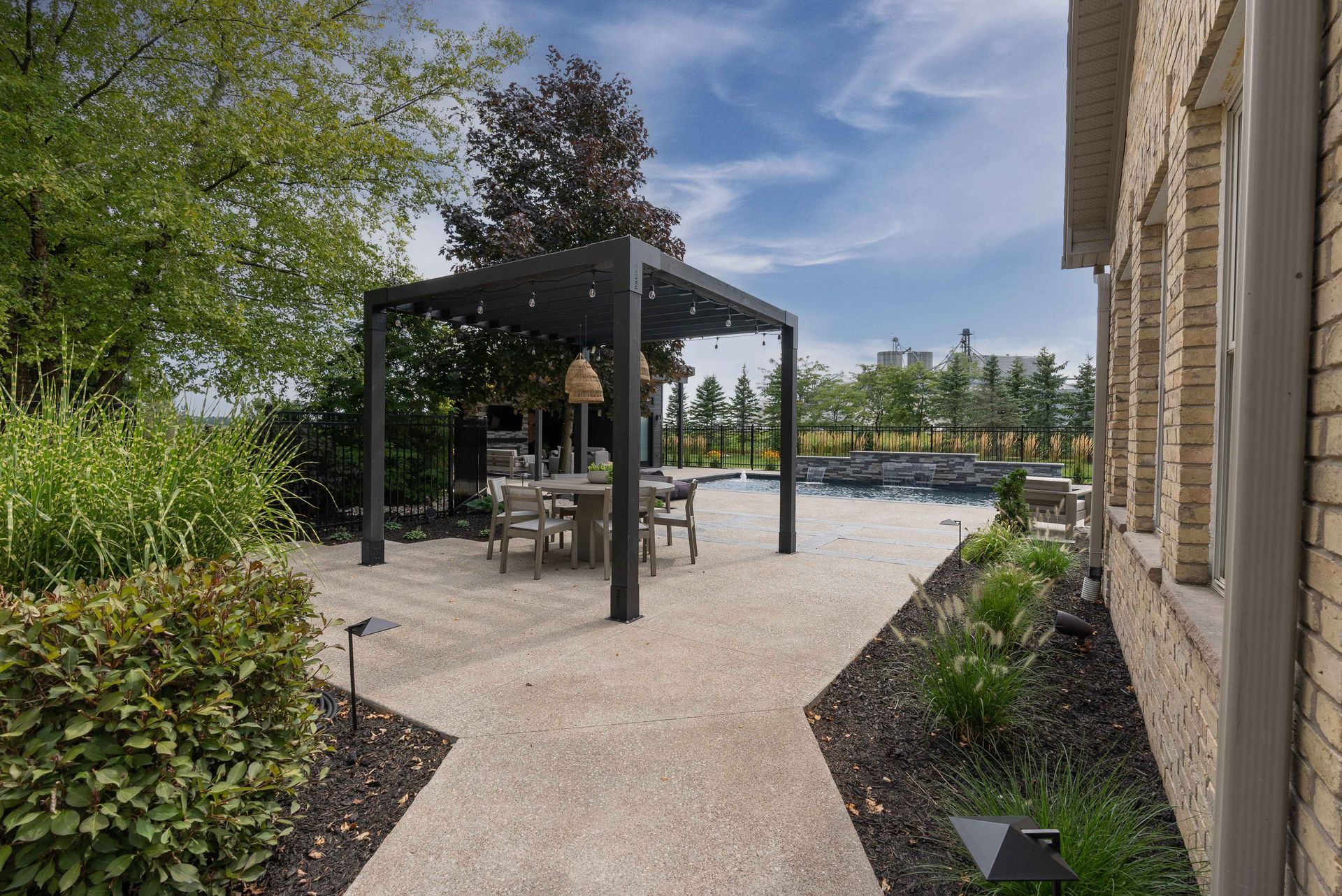 Patio with black pergola, outdoor dining table, gravel path, and landscaped garden beside a stone house