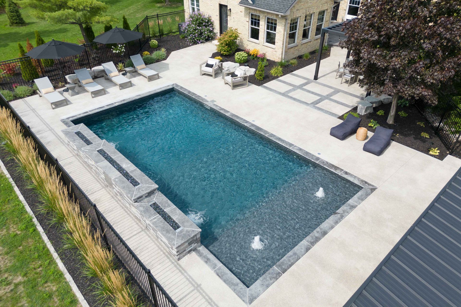 Aerial view of a modern backyard with a rectangular pool, lounge chairs, and a patio beside a house