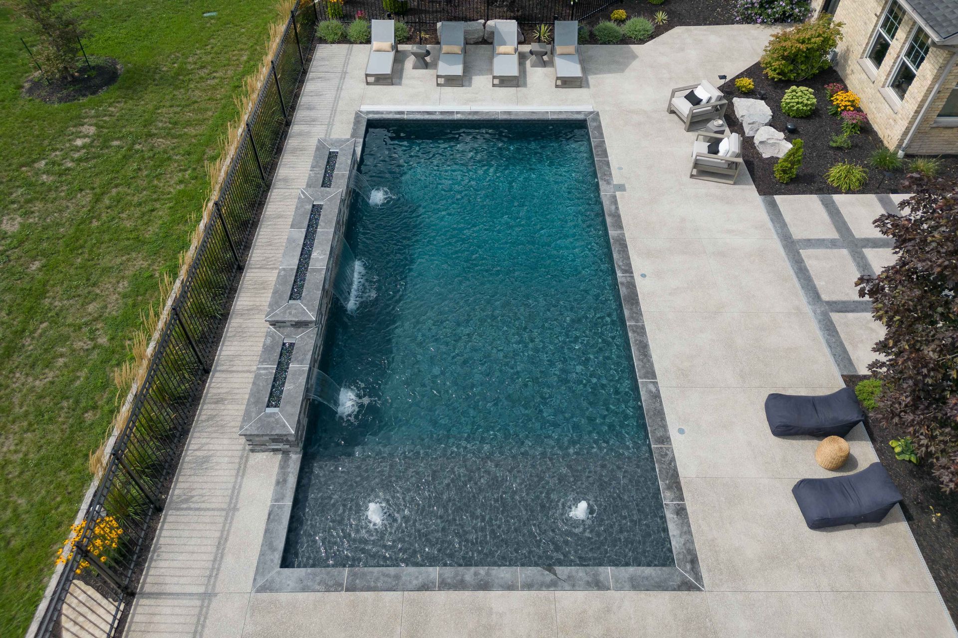 Aerial view of a rectangular backyard pool with lounge chairs and patio seating on a stone deck.