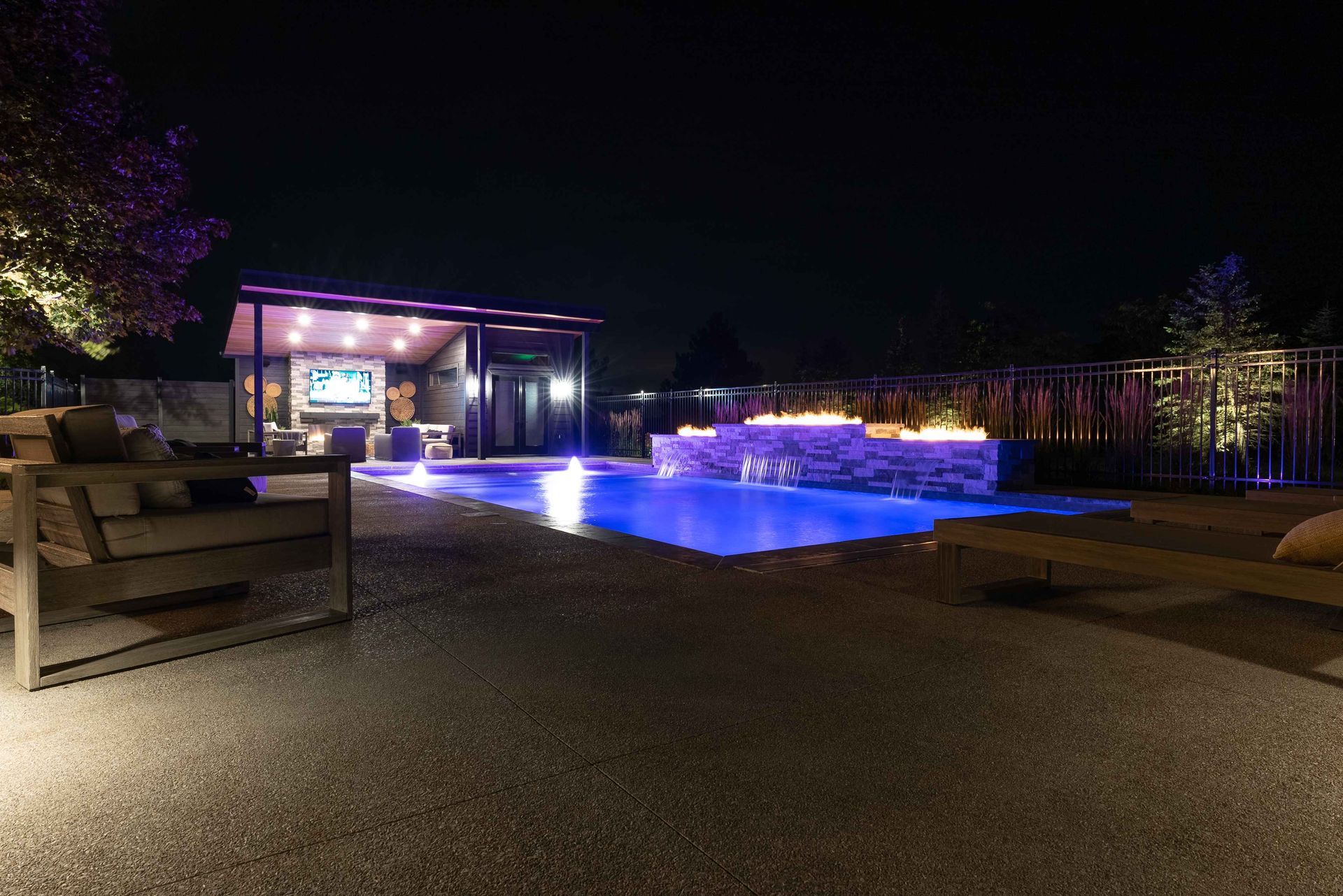 Nighttime outdoor pool lit blue beside a modern building with purple lights