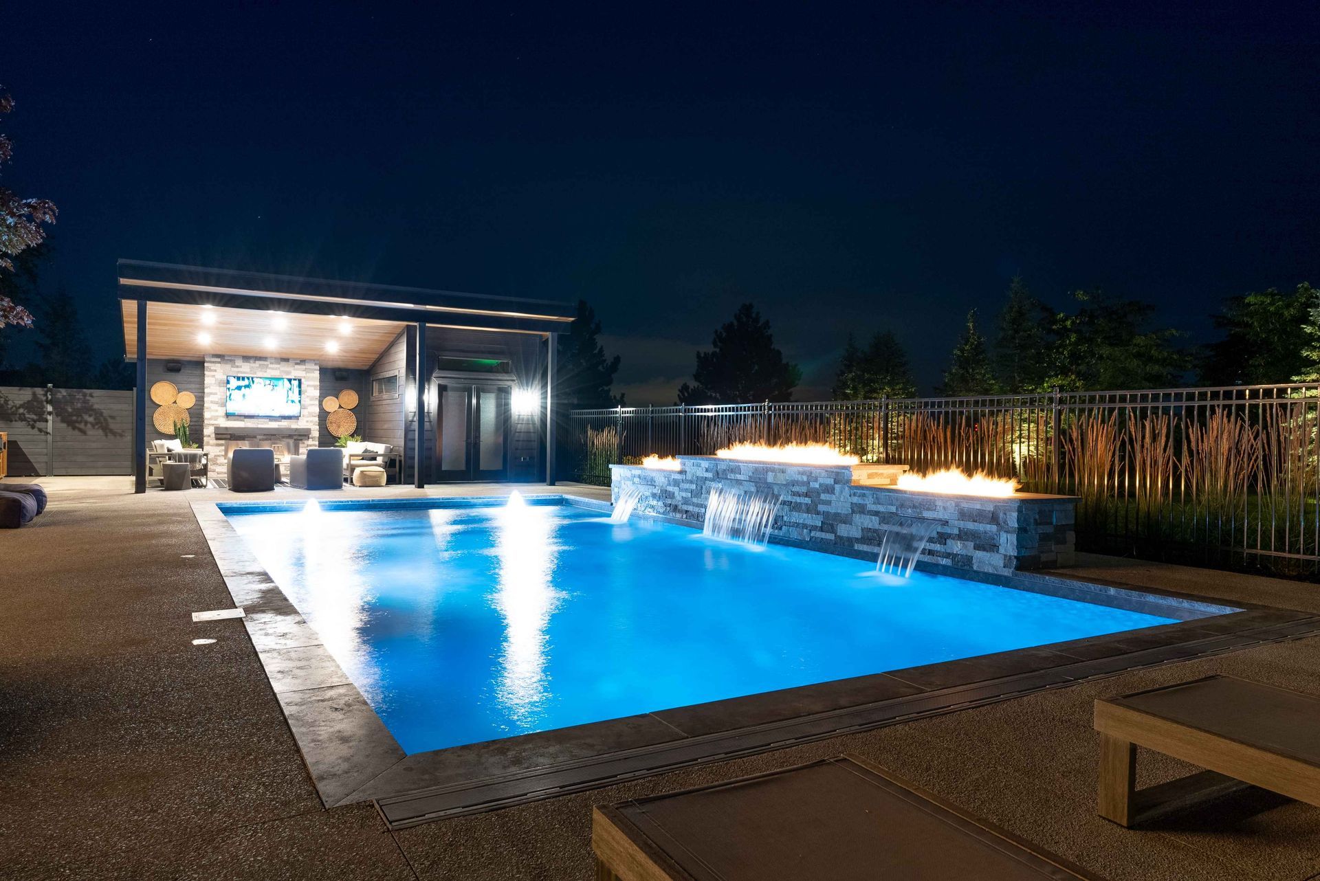 Nighttime poolside patio with a glowing blue swimming pool and a lit outdoor lounge area
