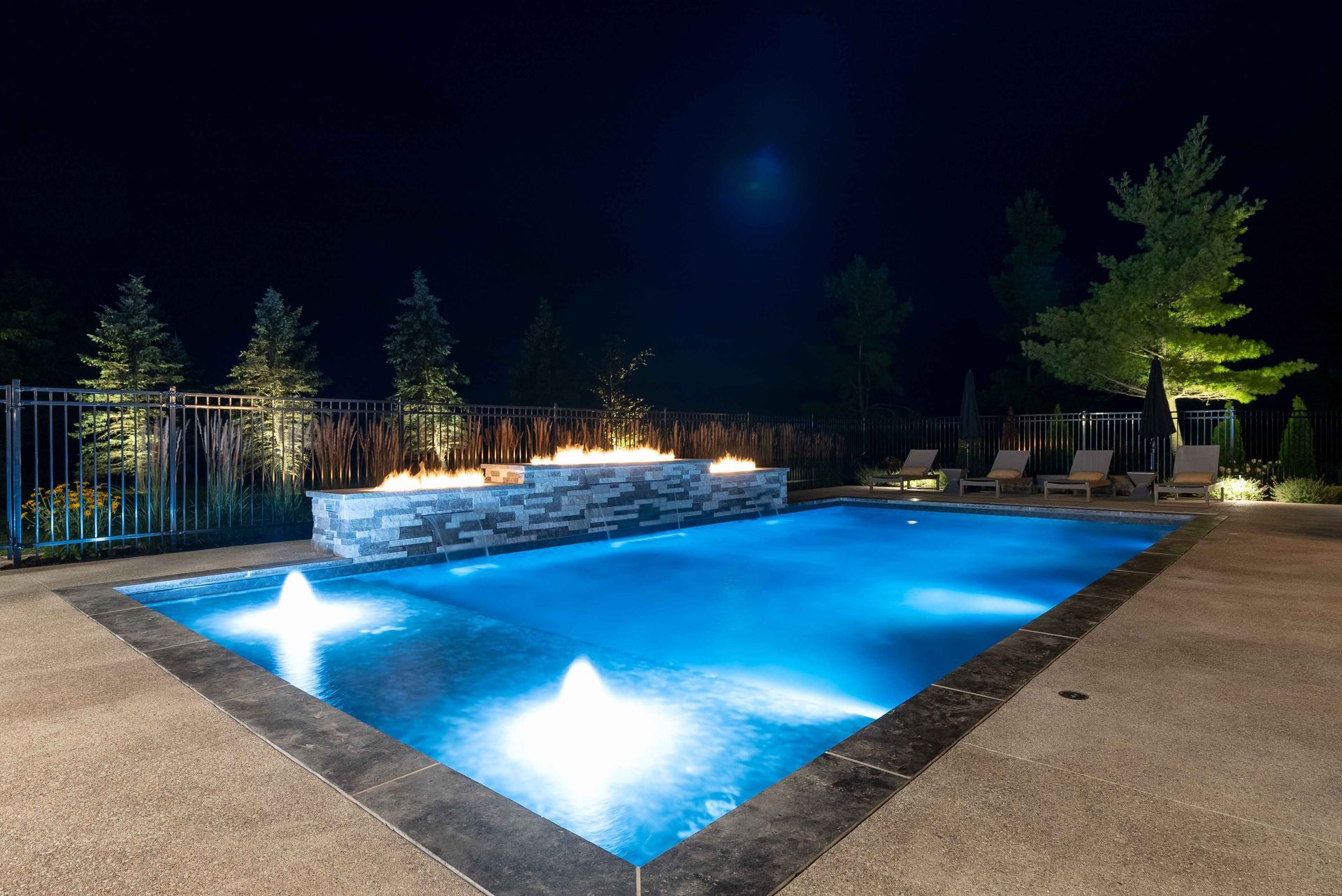 Illuminated outdoor swimming pool at night with bright blue water and surrounding trees