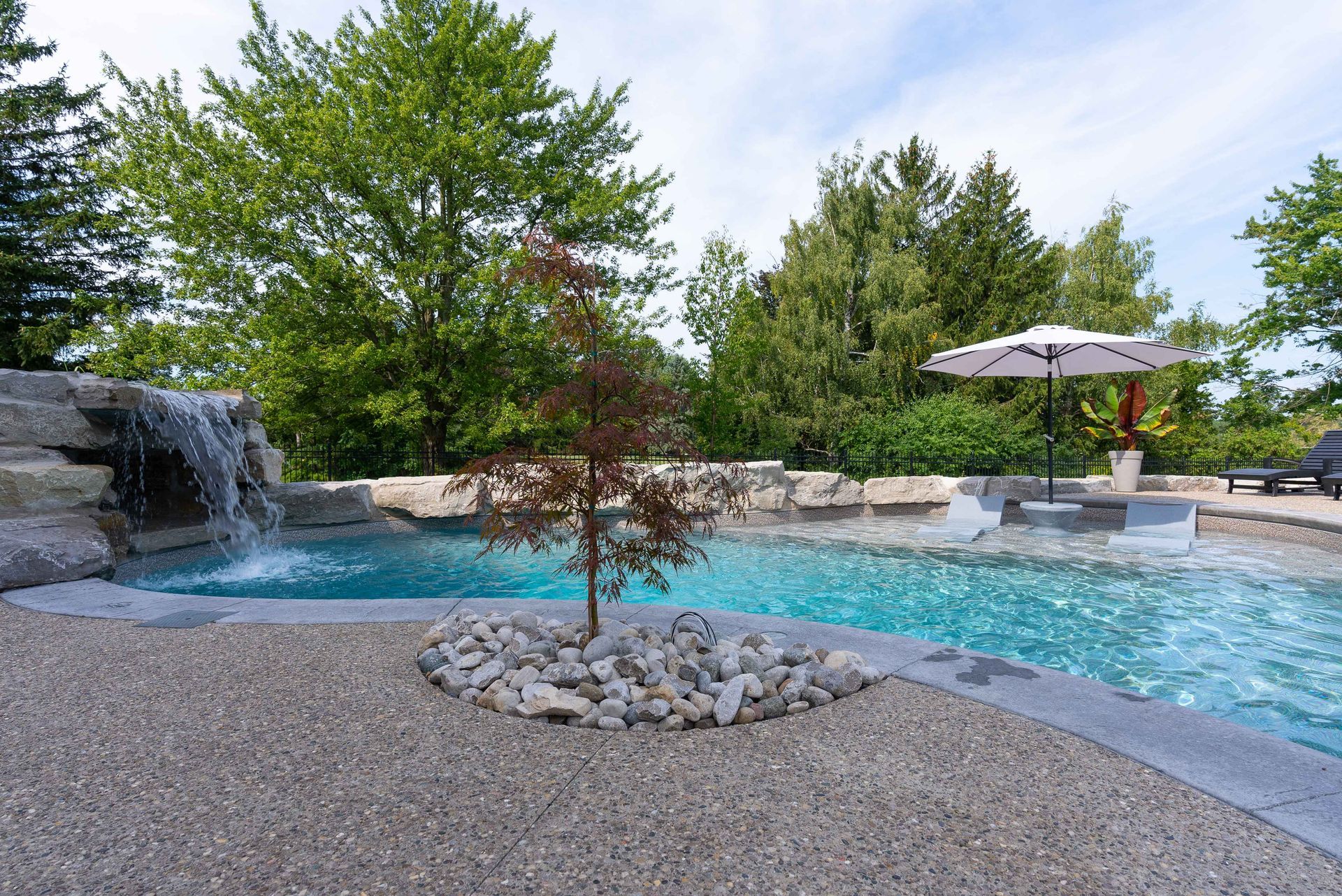 Backyard pool with waterfall, stone edging, and lounge chairs under an umbrella
