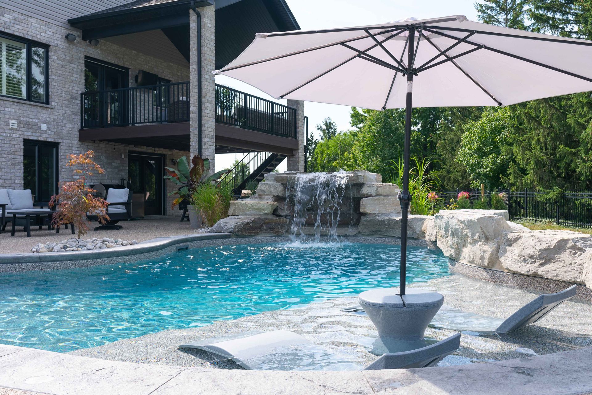 Backyard pool with waterfall, patio, and large umbrella beside a modern house