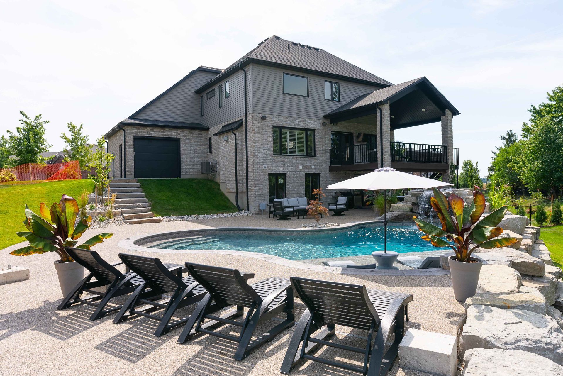 Modern gray house with backyard pool, lounge chairs, and patio seating under umbrellas