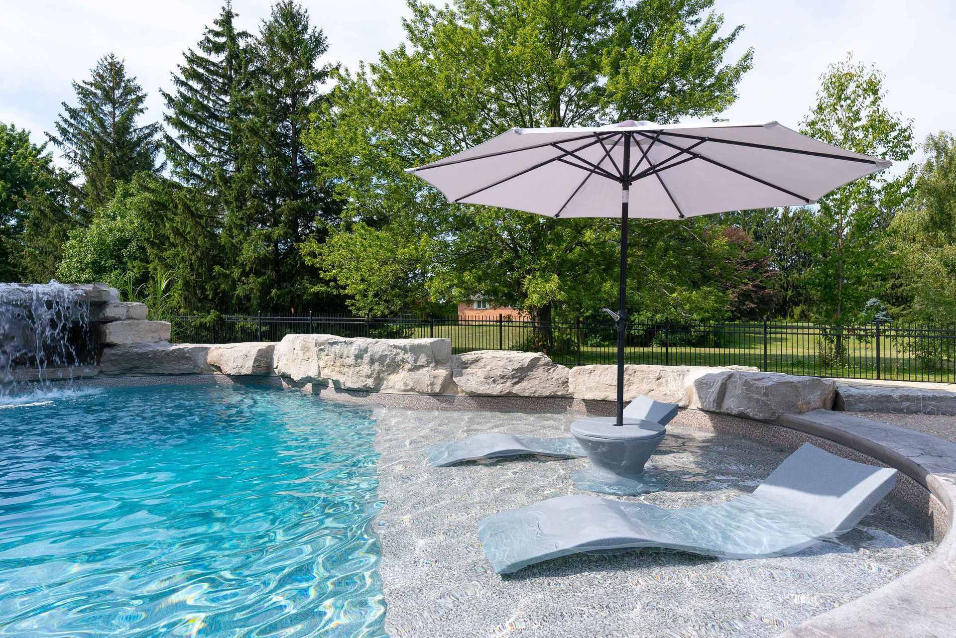 Backyard pool with lounge chairs and umbrella beside turquoise water and trees