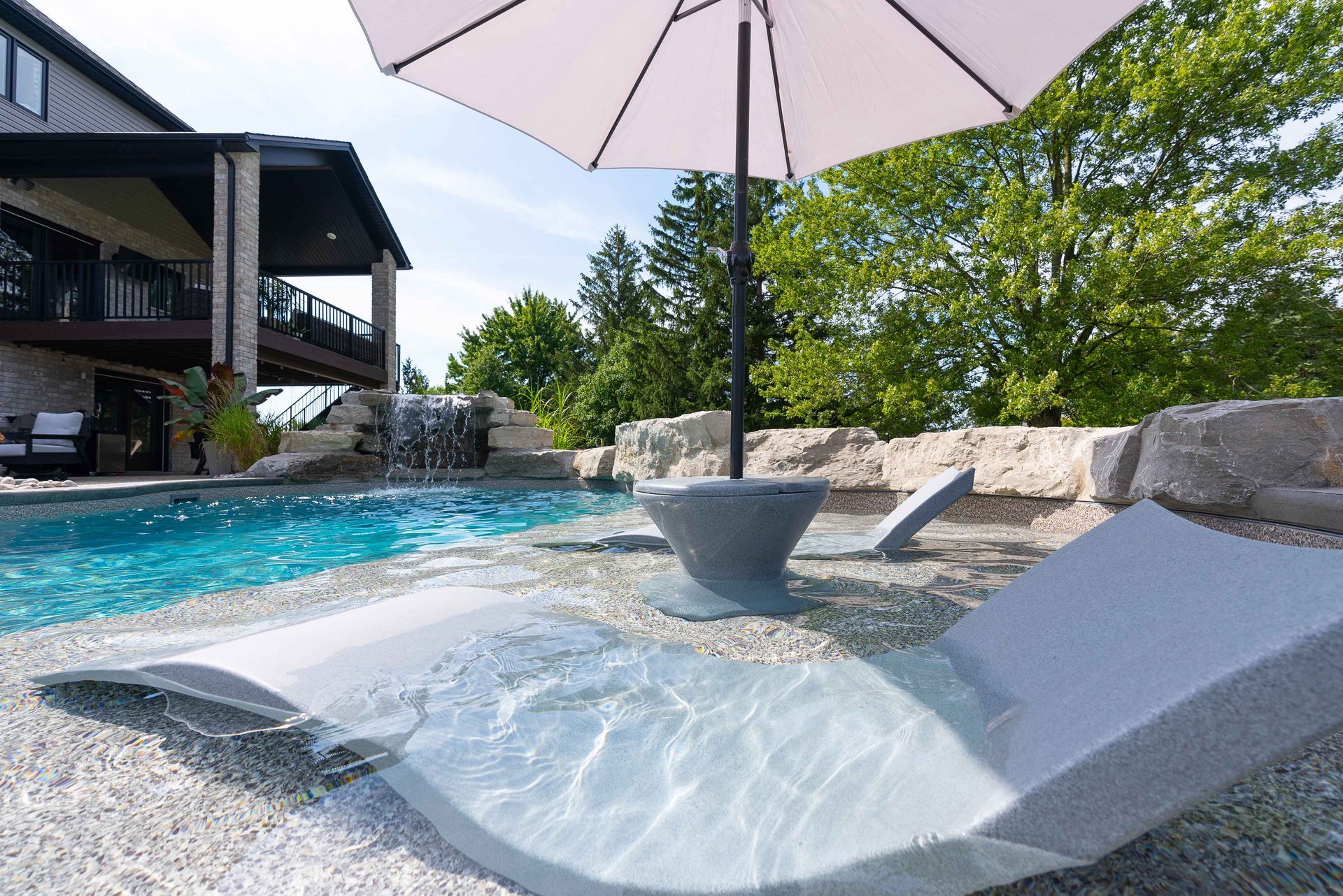 Luxury poolside lounge chair beside a blue swimming pool with umbrella and stone landscaping