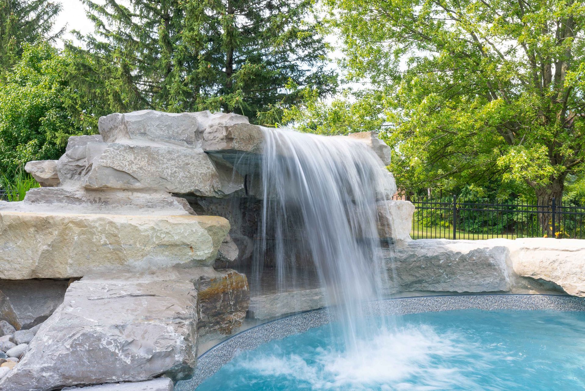 Waterfall spilling from a stone ledge into a clear blue pool, surrounded by lush green trees