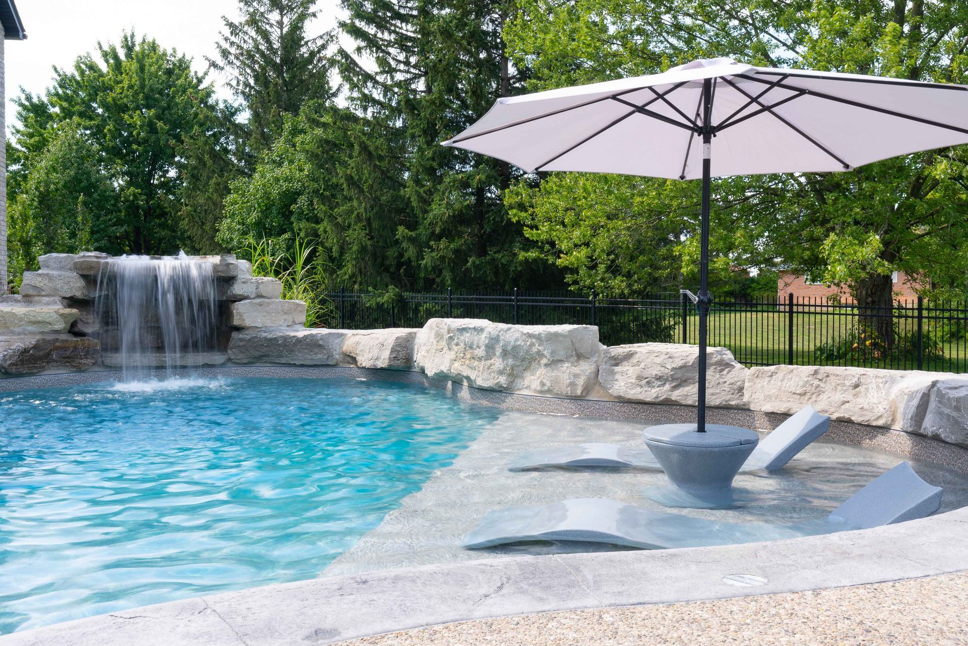 Backyard pool with waterfall, lounge chairs, and a purple umbrella beside turquoise water
