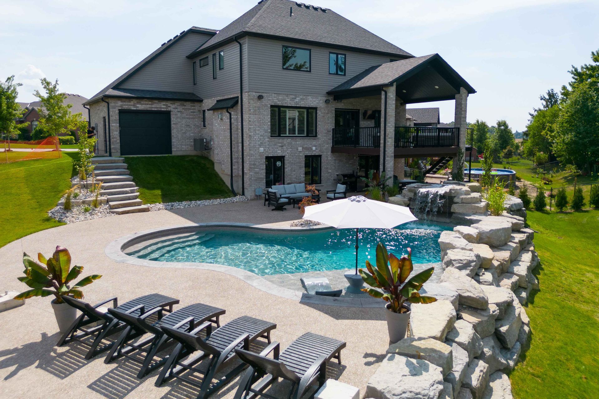 Luxury stone house with a backyard pool, patio seating, and landscaped rock garden