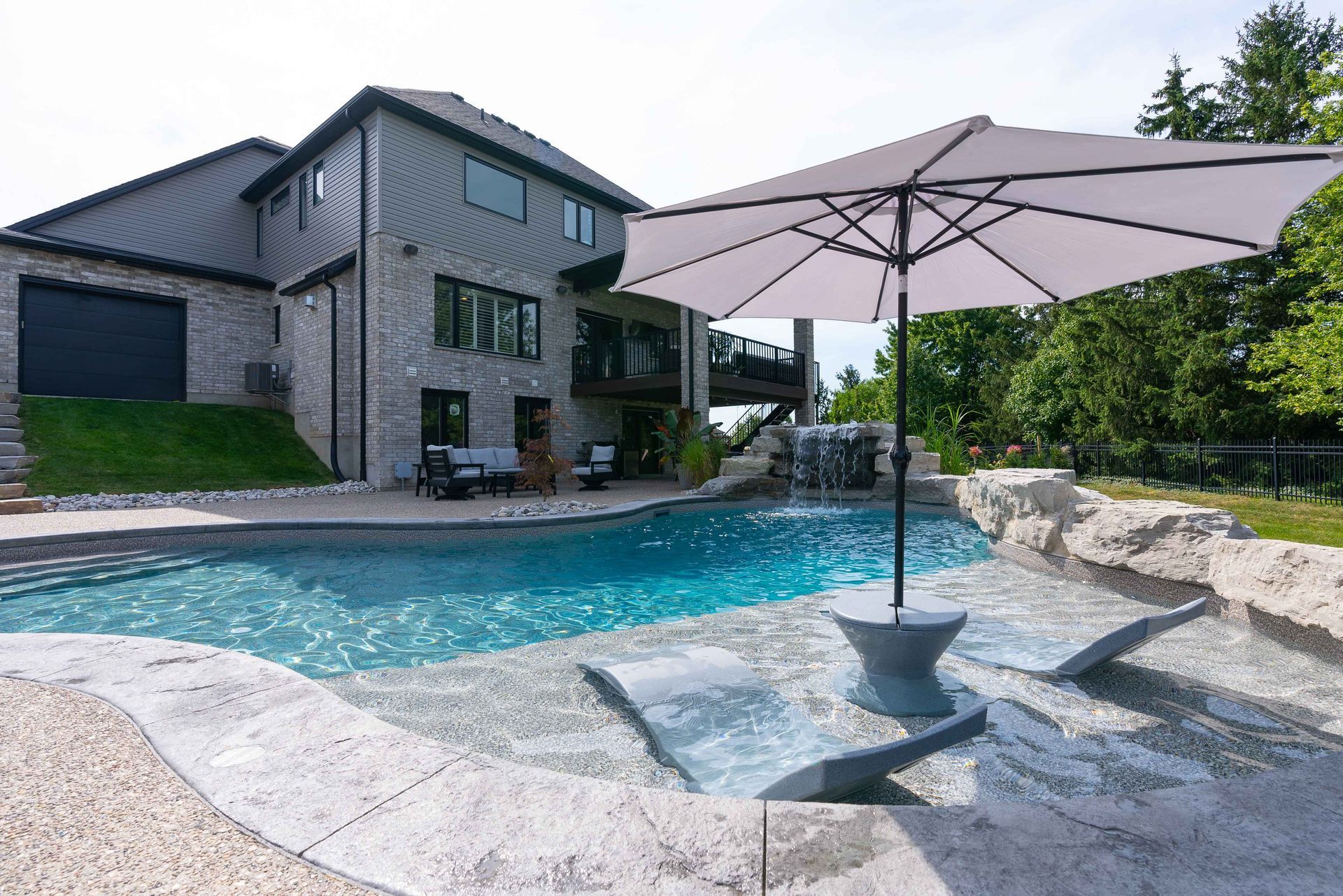 Backyard pool with a patio umbrella beside a modern gray house