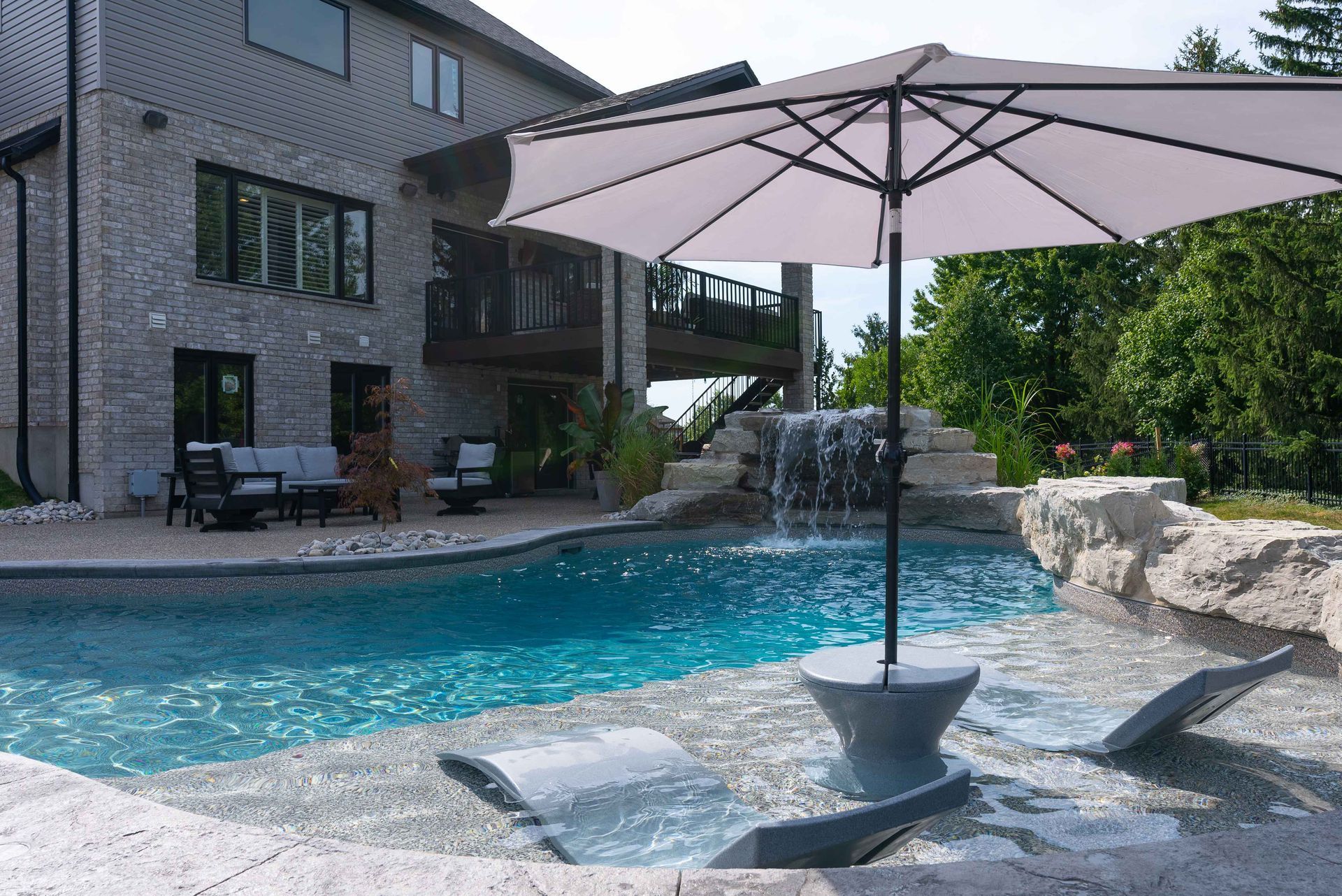 Backyard pool with patio umbrella, lounge chairs, and a modern house in the background