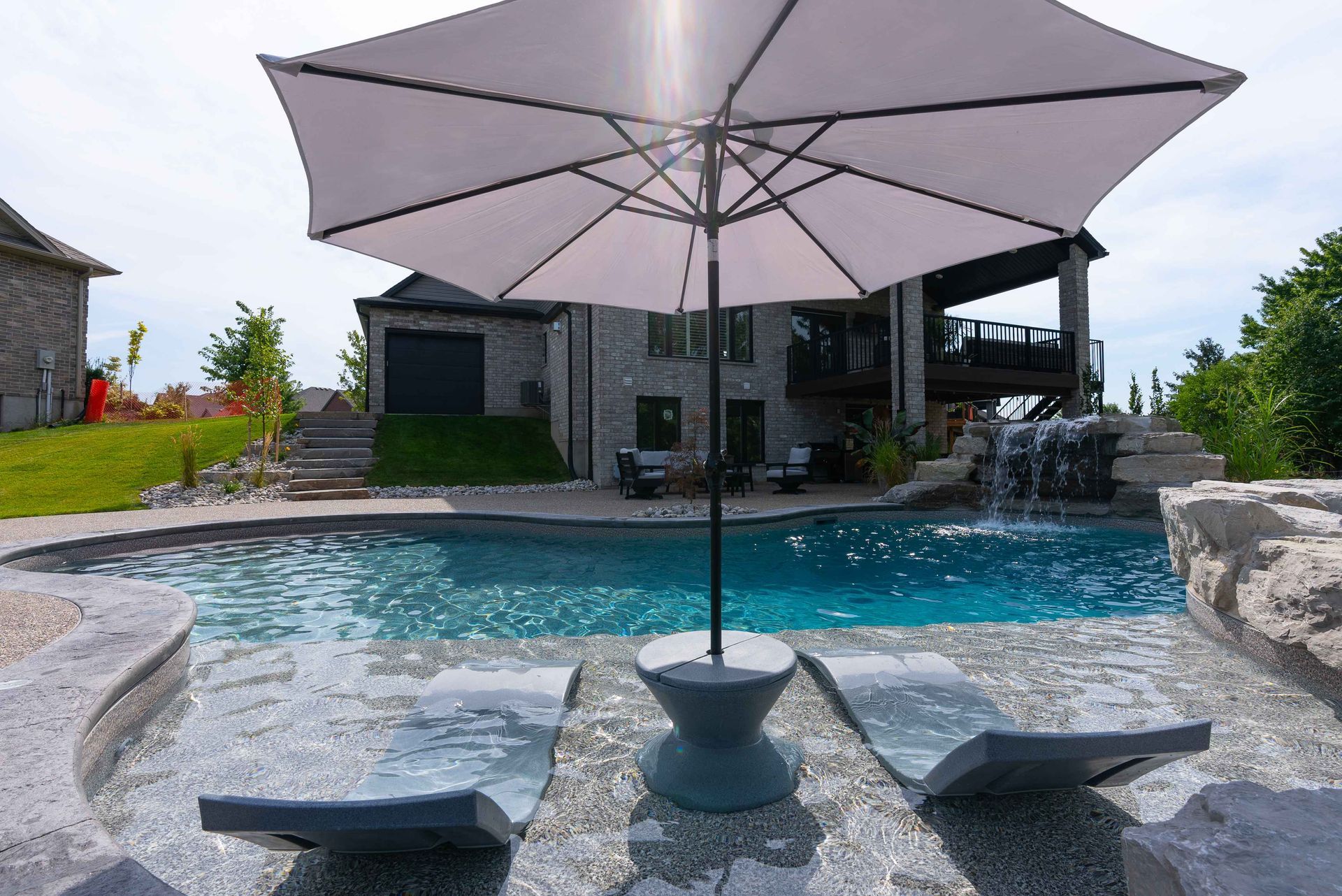 Backyard pool with patio umbrella and lounge chairs beside a modern house