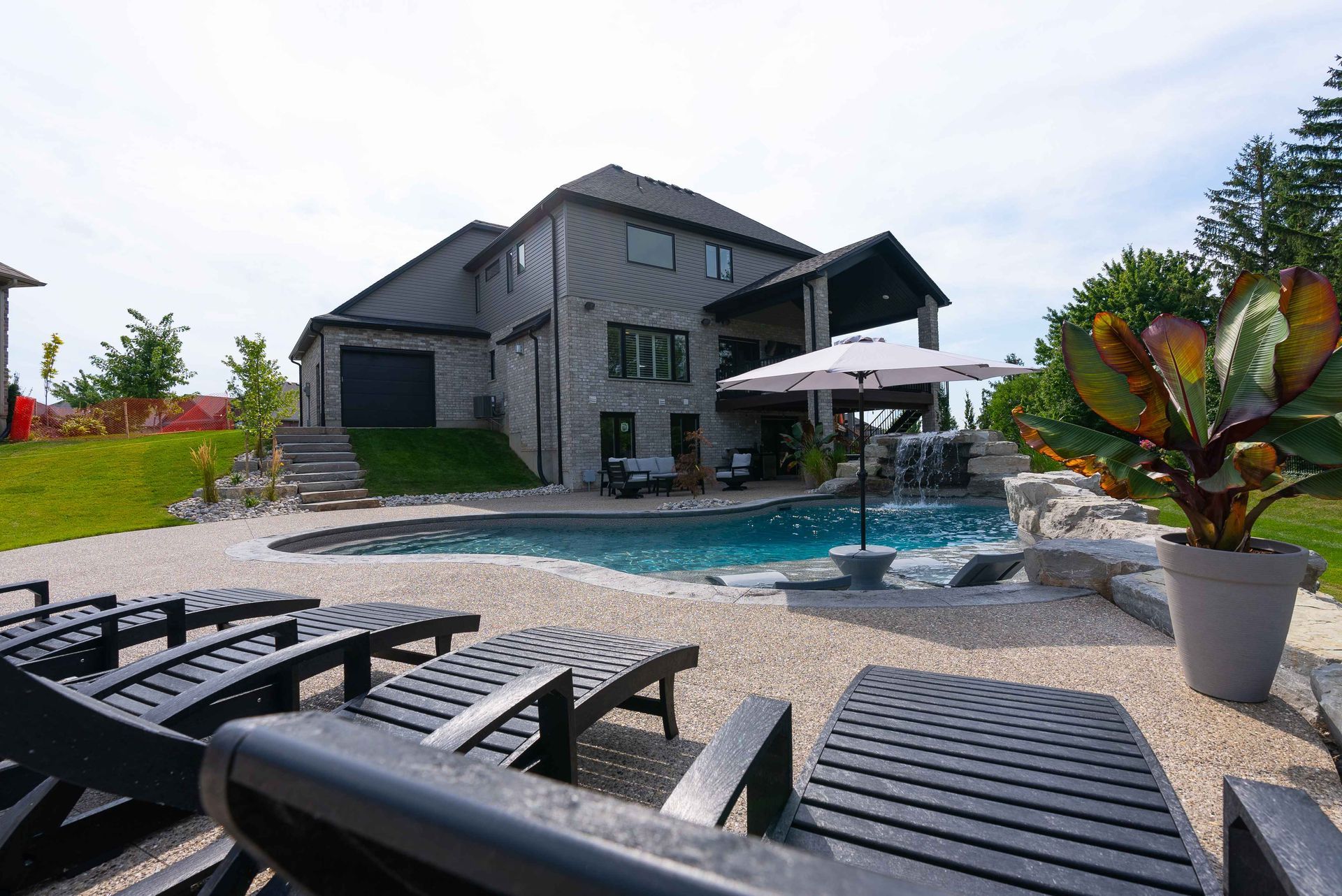 Modern house with a swimming pool, lounge chairs, and tropical plants in the backyard
