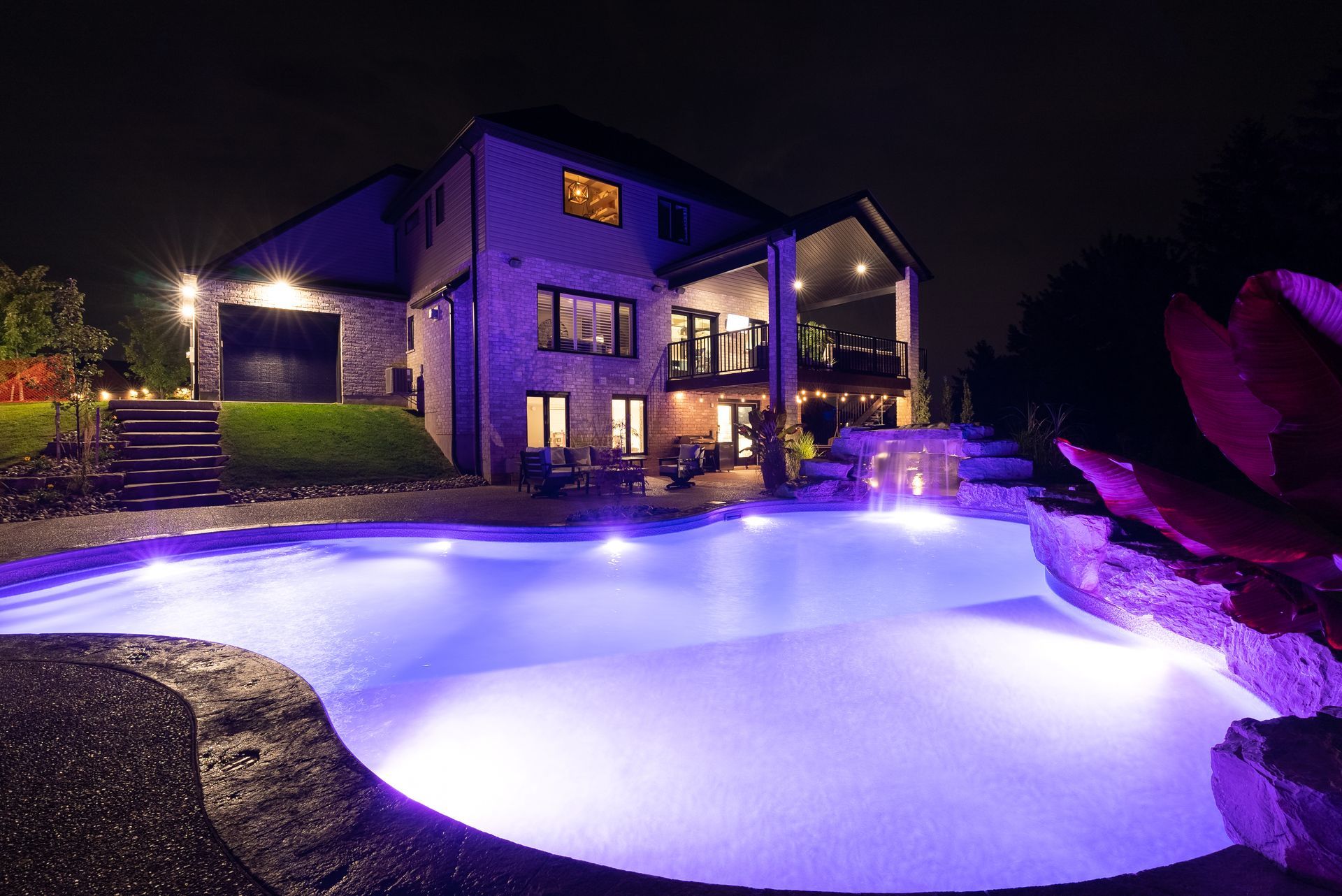 Modern house at night with a lit pool and purple-blue lighting