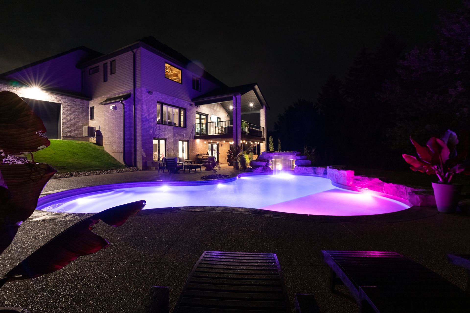 Luxury house with glowing purple and blue lit backyard pool at night