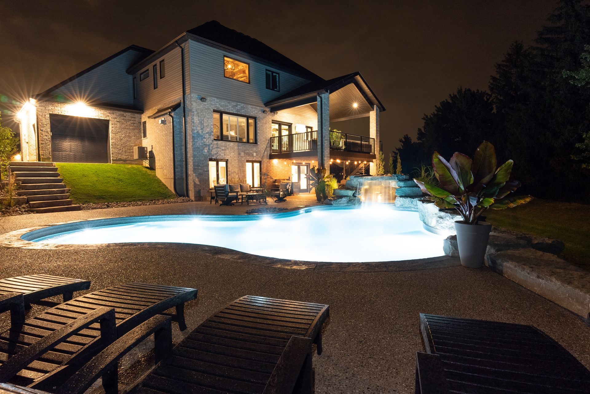 Nighttime view of a lit luxury house with a glowing pool and patio seating