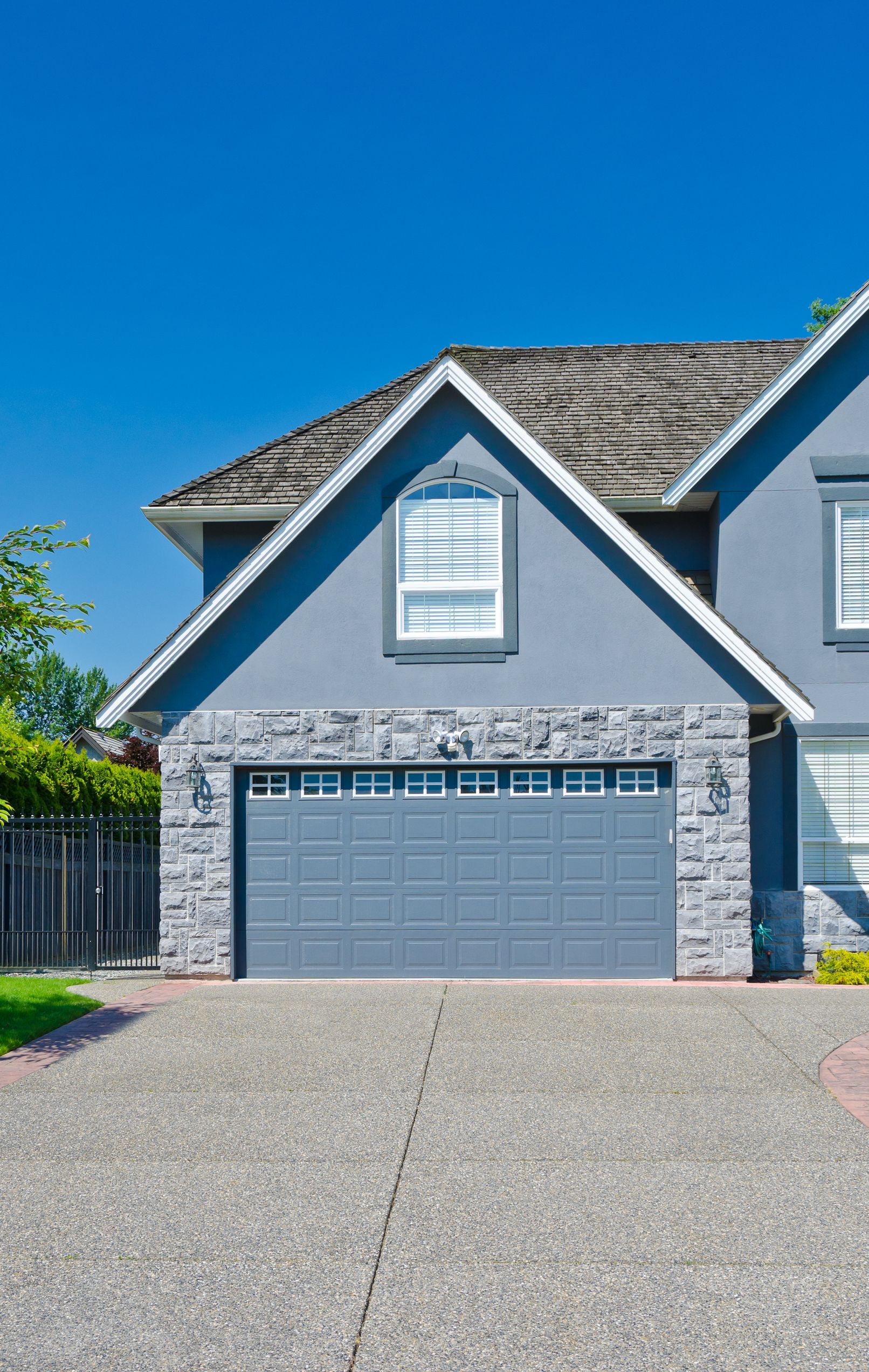 A blue house with a gray stone-accented two-car garage and a paved driveway under a clear blue sky.
