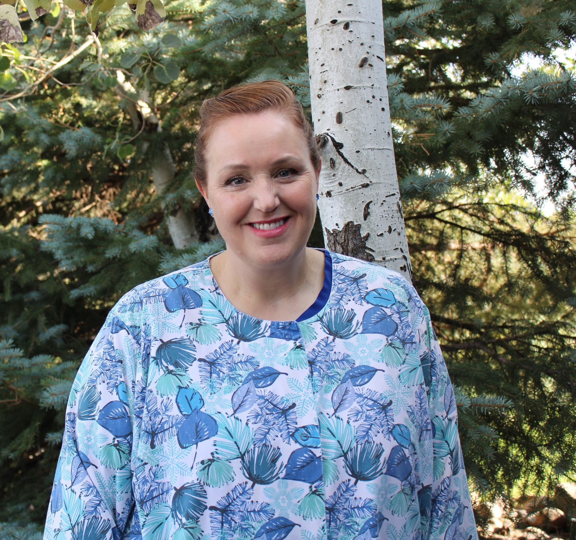 A woman in a floral shirt is smiling in front of trees