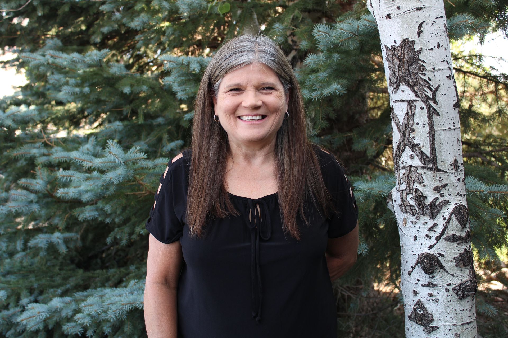 A Woman in A Black Shirt Is Standing in Front of A Tree.