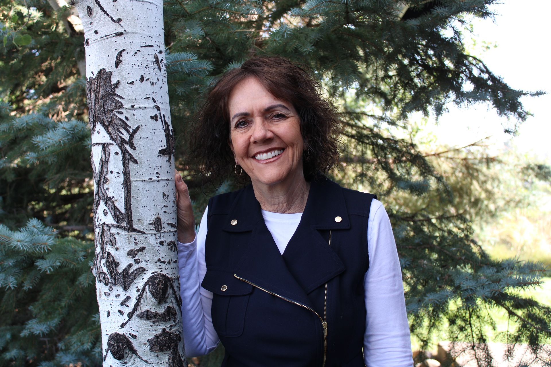 A woman is standing next to a tree and smiling.