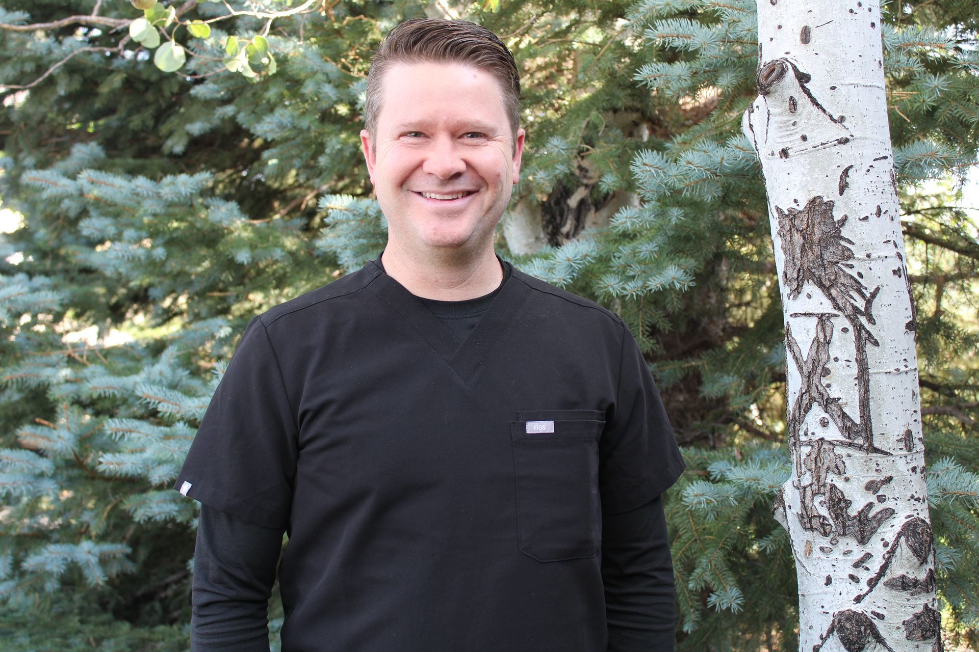 A Man in A Black Shirt Is Standing in Front of A Tree.