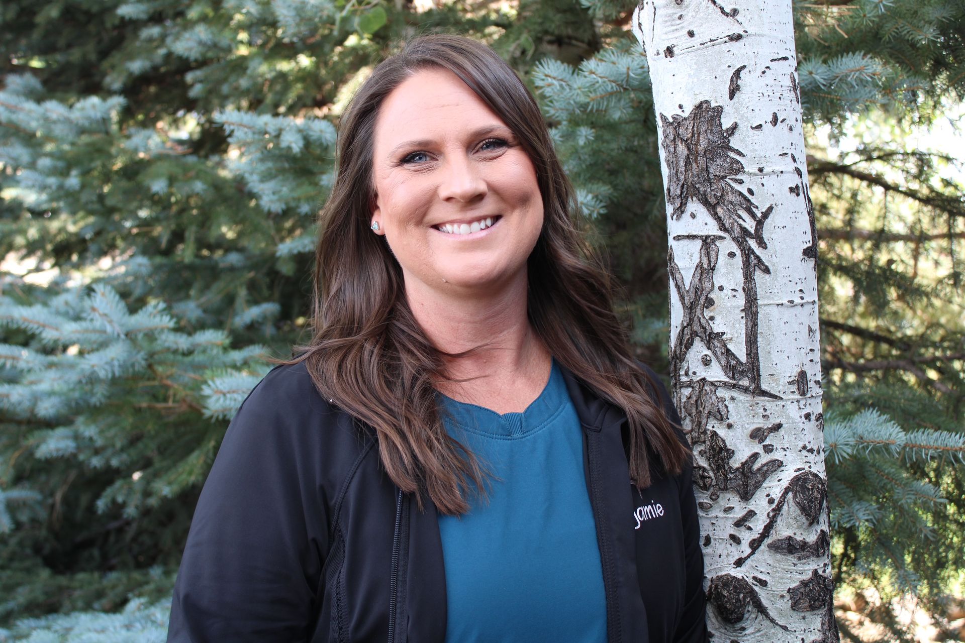 A woman is standing next to a tree and smiling.