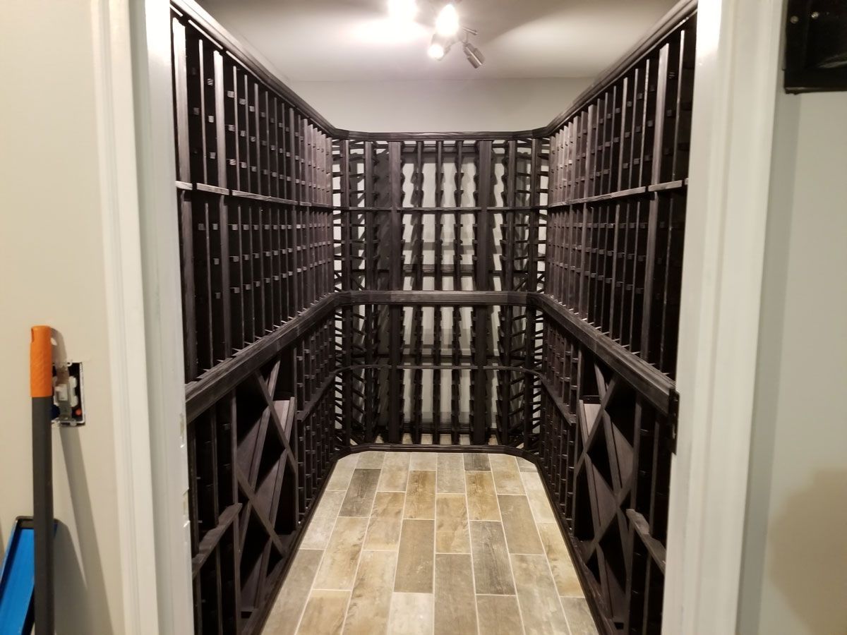 A large wine cellar with lots of shelves and a shovel in the doorway.
