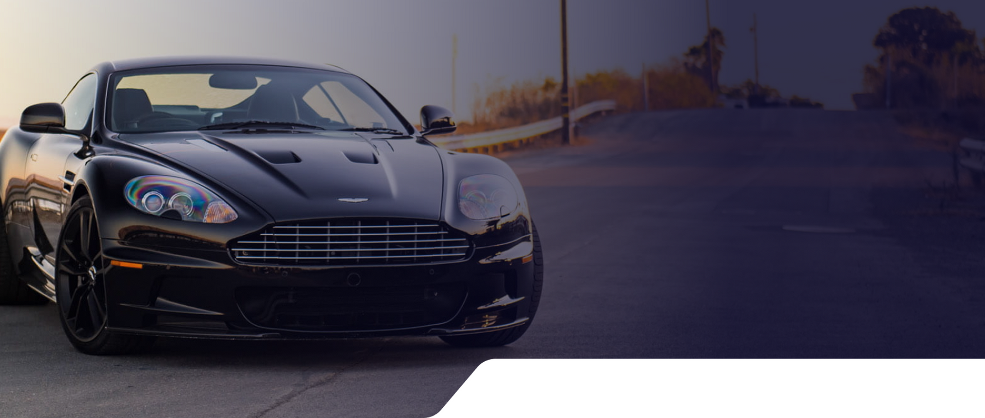 A white sports car is driving down a road at sunset.